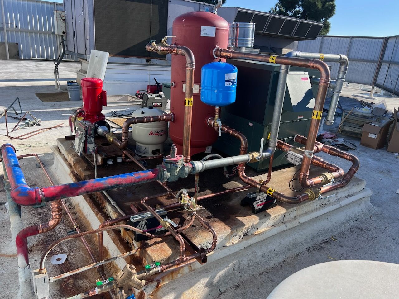 A rooftop industrial water heating system with red and copper pipes, tanks, and other components.
