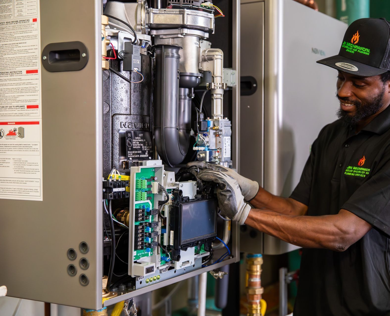 A smiling man wearing a hat works on a furnace.
