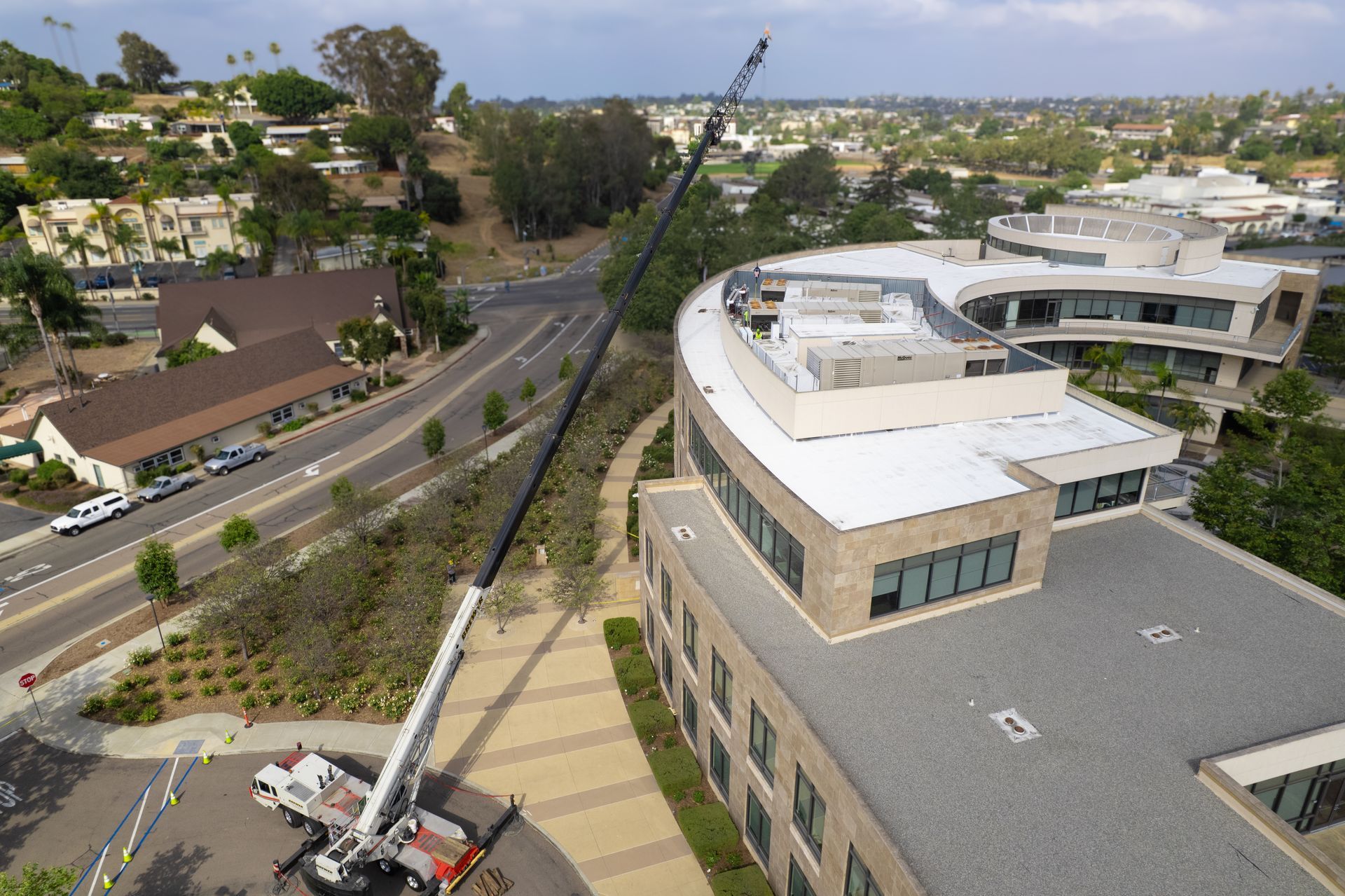 Aerial view of a road beside commercial buildings, with a crane lifting a boiler.
