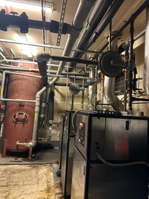 Interior of a mechanical room with pipes, tanks, and machinery, mostly gray and brown.