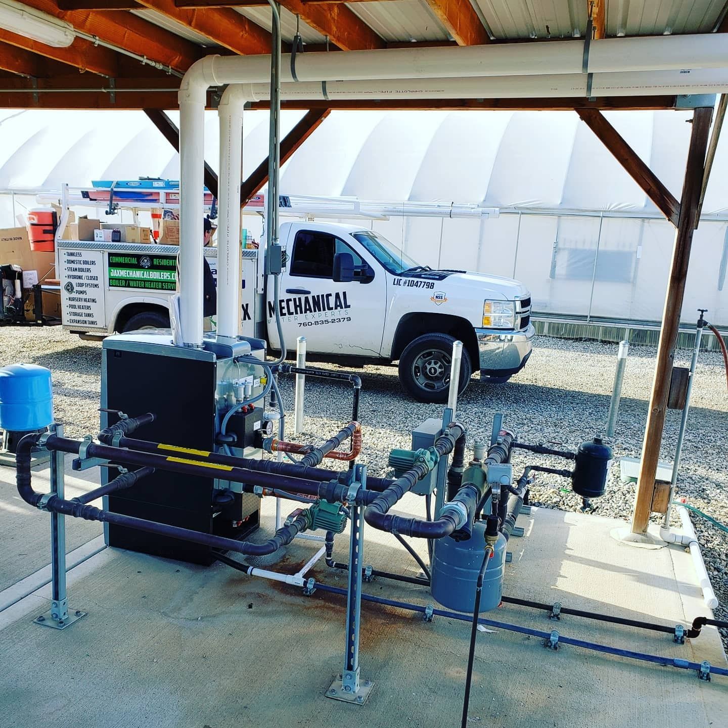 Plumbing and HVAC equipment, including a water heater, pipes, and gauges, are installed outside. A work truck sits behind it.