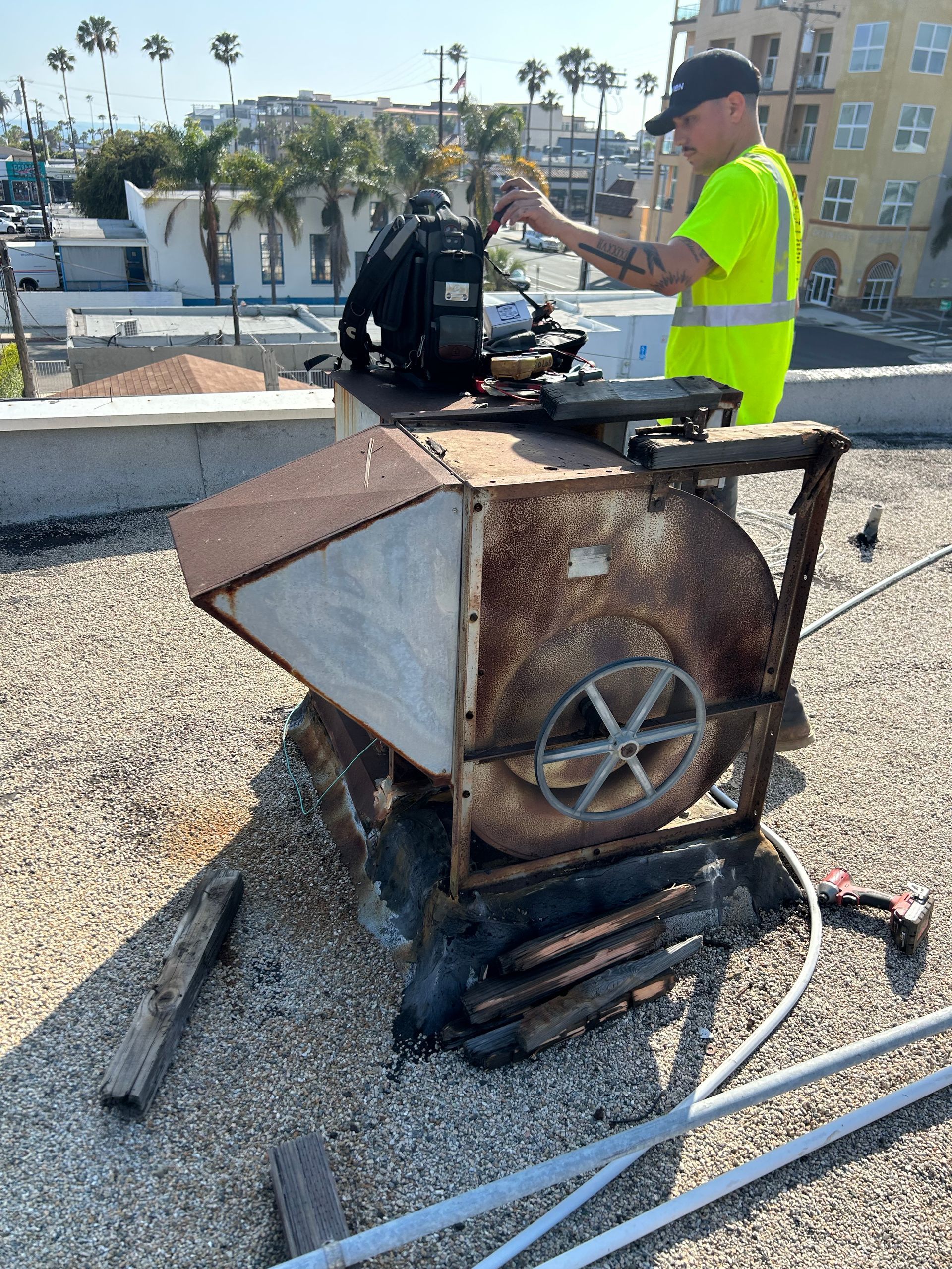 A white rooftop HVAC unit unit with dark soot, on a gray roof, with green hillside in the background.