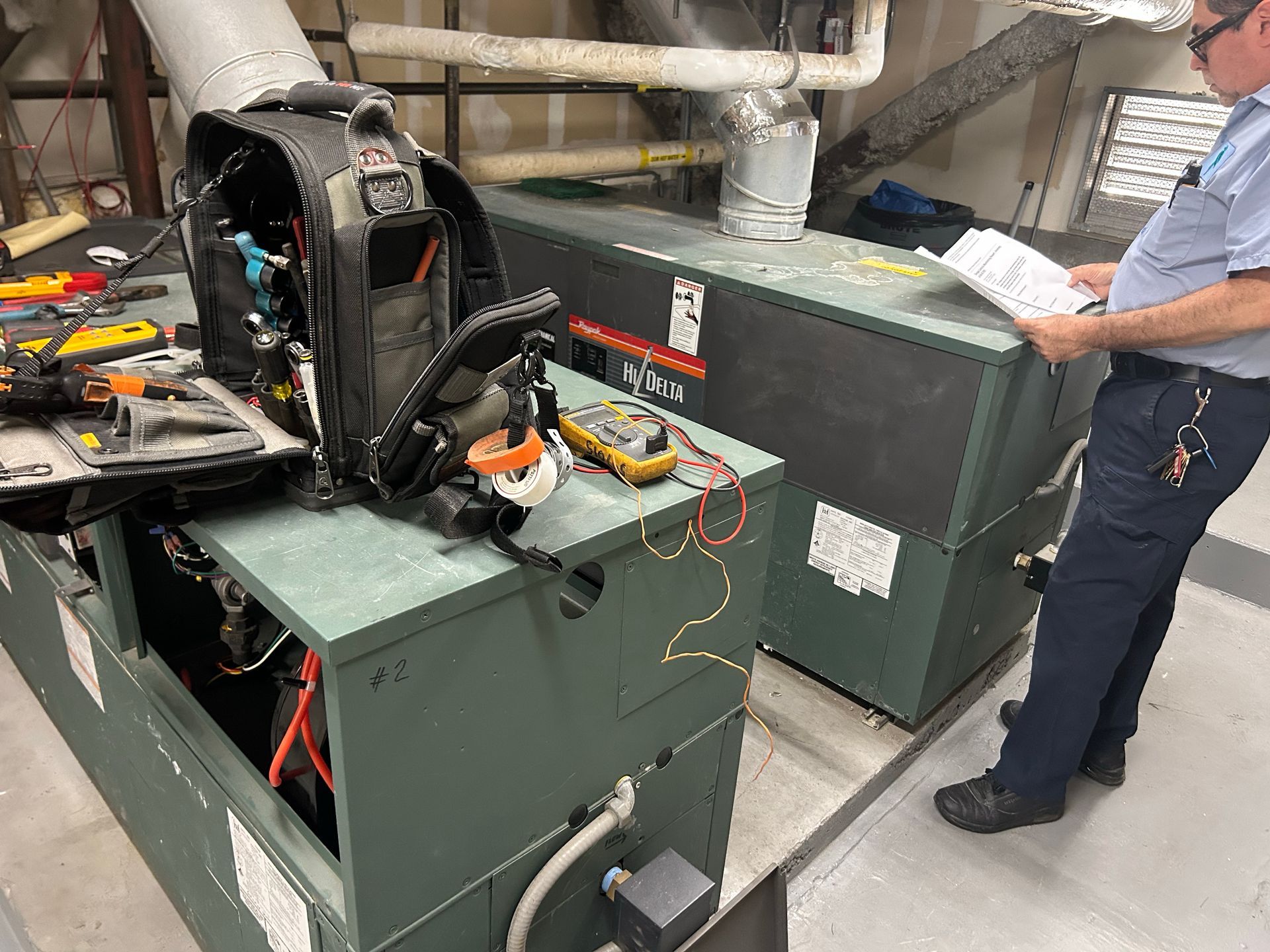 HVAC technician inspects a furnace, tools and equipment nearby. Interior setting.