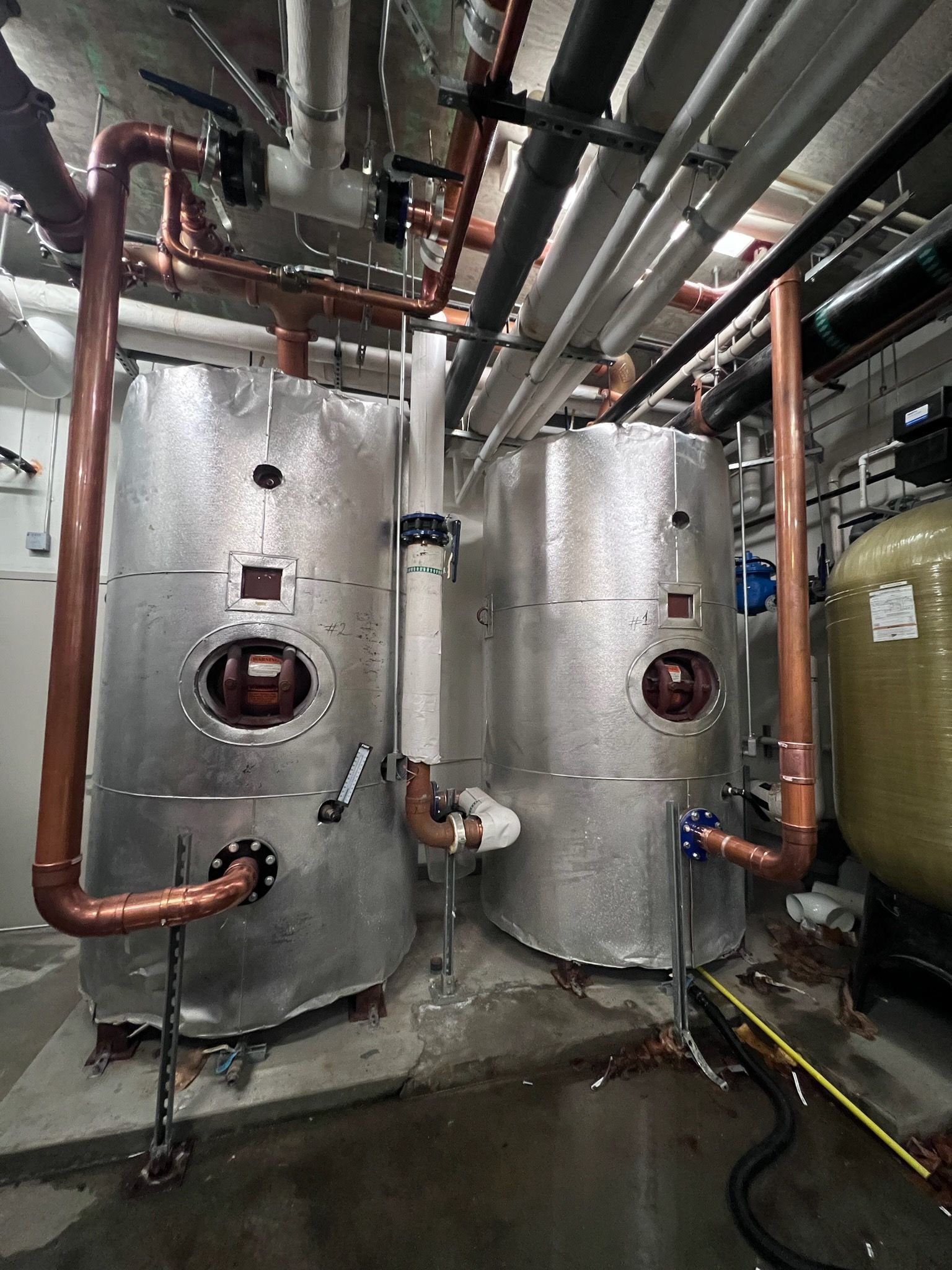 Two large silver insulated tanks with copper piping in an industrial setting. Piping runs overhead.