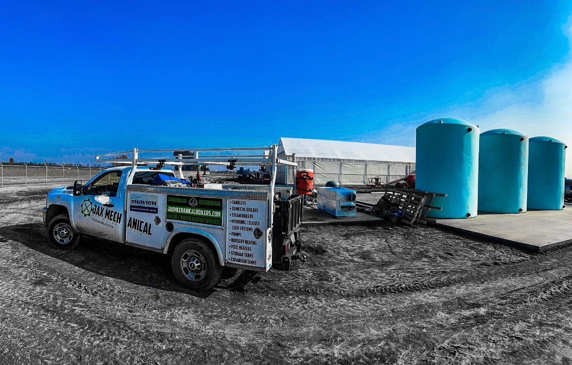 White work truck parked near blue water tanks and a white tent under a bright blue sky.
