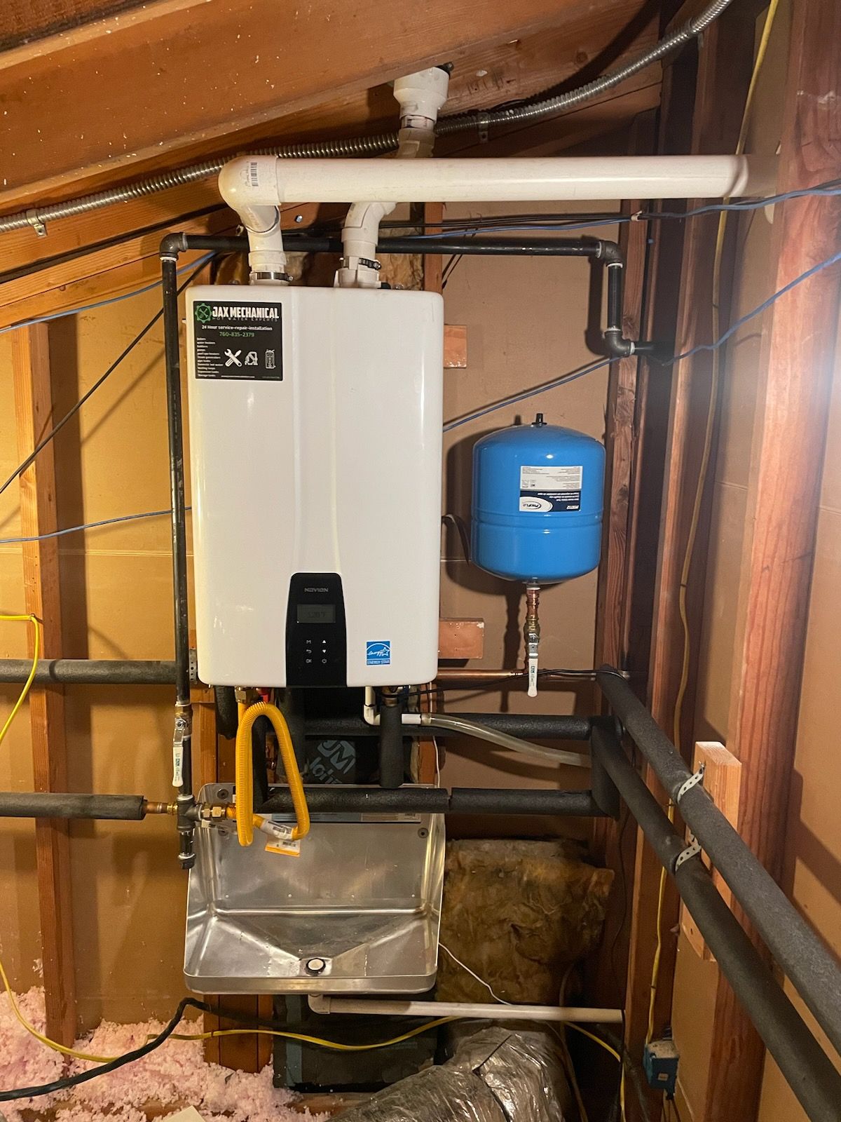A wall-mounted, white tankless water heater with a blue expansion tank, installed in a utility room.