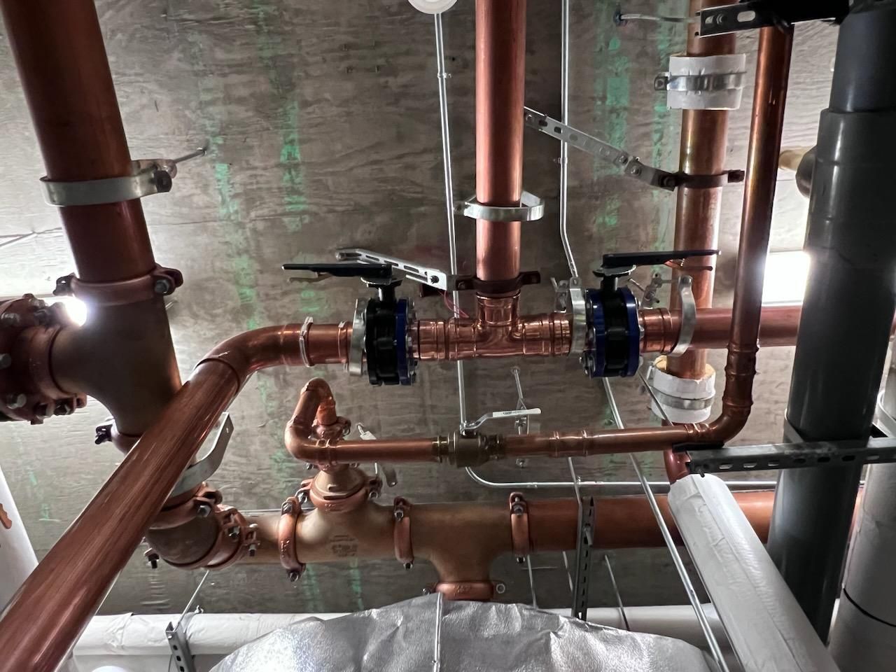 Copper pipes with black-handled valves and white supports running along a concrete ceiling.