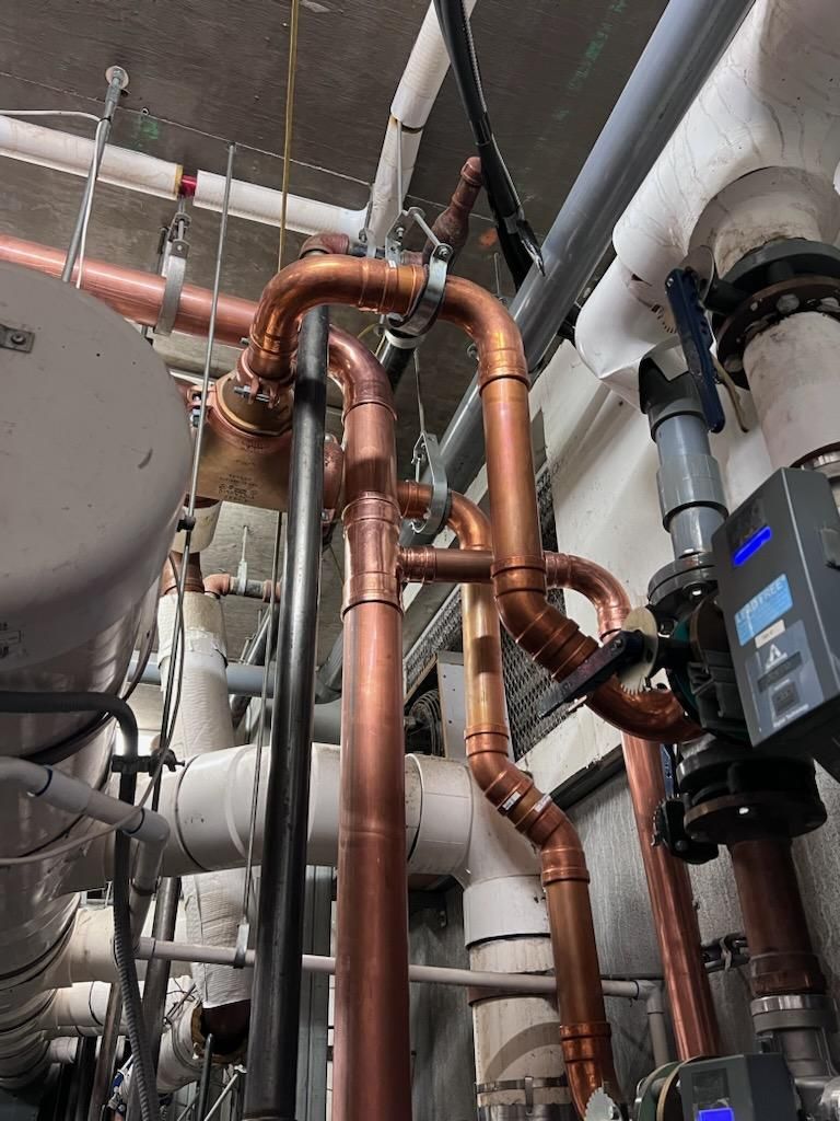 Copper pipes with various bends and connections, part of a plumbing system in a mechanical room.