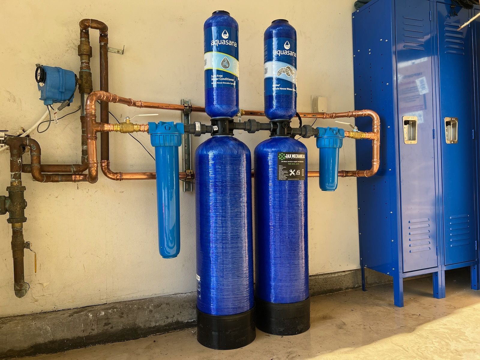 Water filtration system with blue tanks, copper pipes, and a blue cabinet against a beige wall.