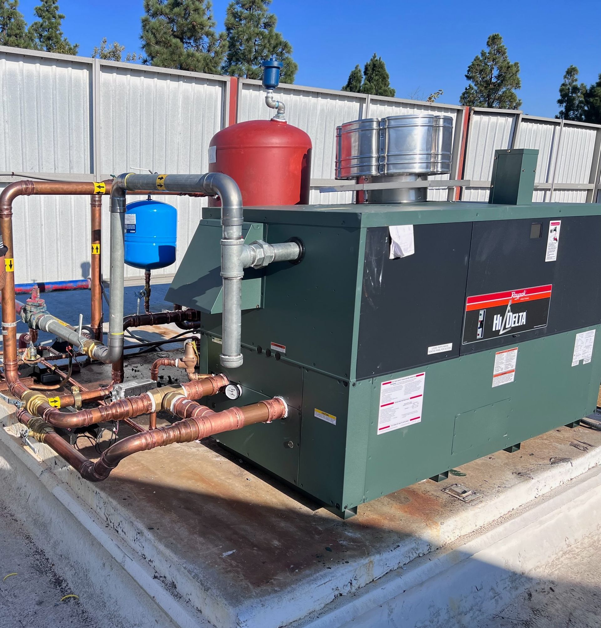 A rooftop HVAC system with copper piping, a red expansion tank, and a blue water tank.
