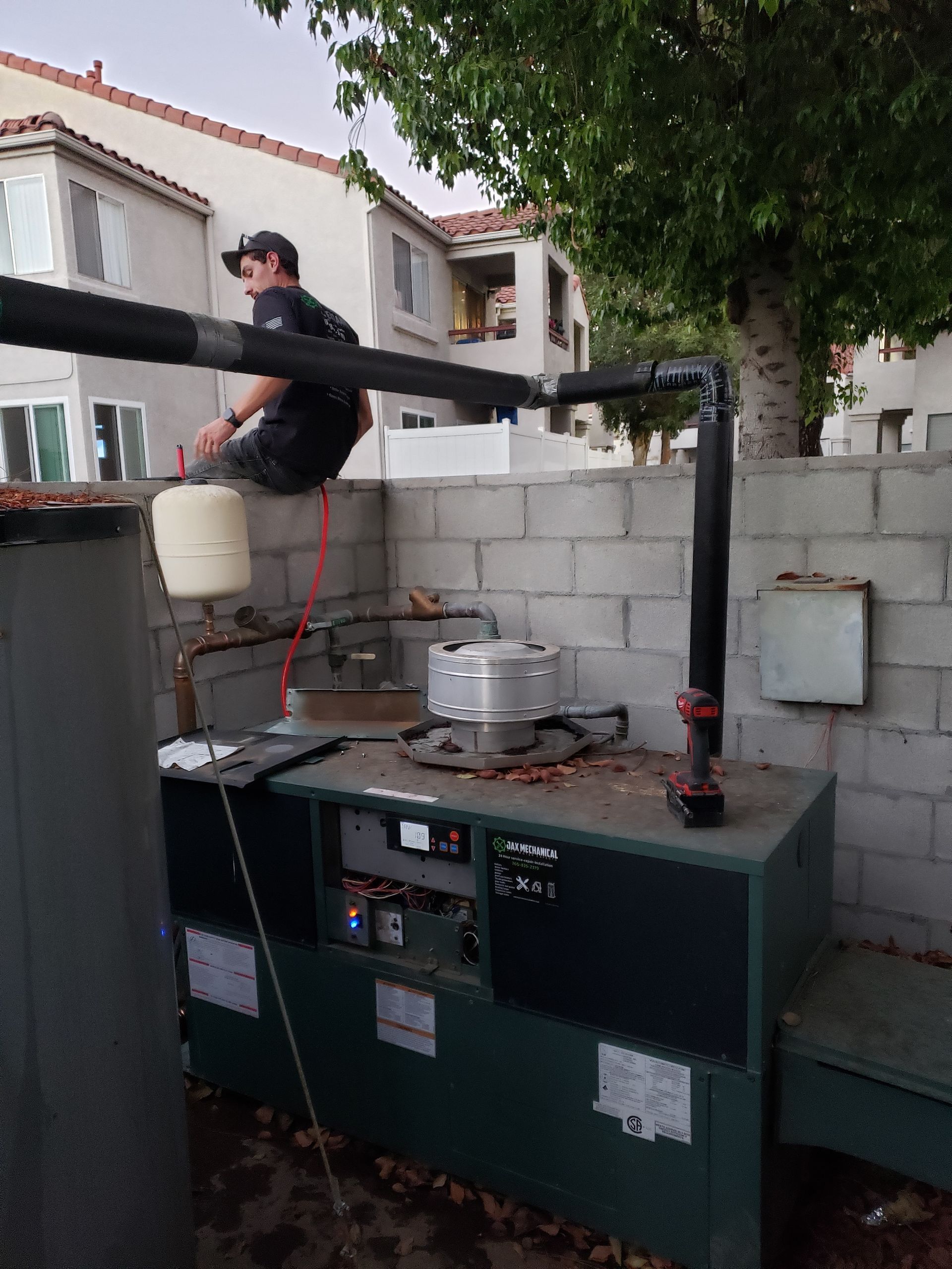 A person sits atop a large green machine, likely for plumbing, in a fenced outdoor area.