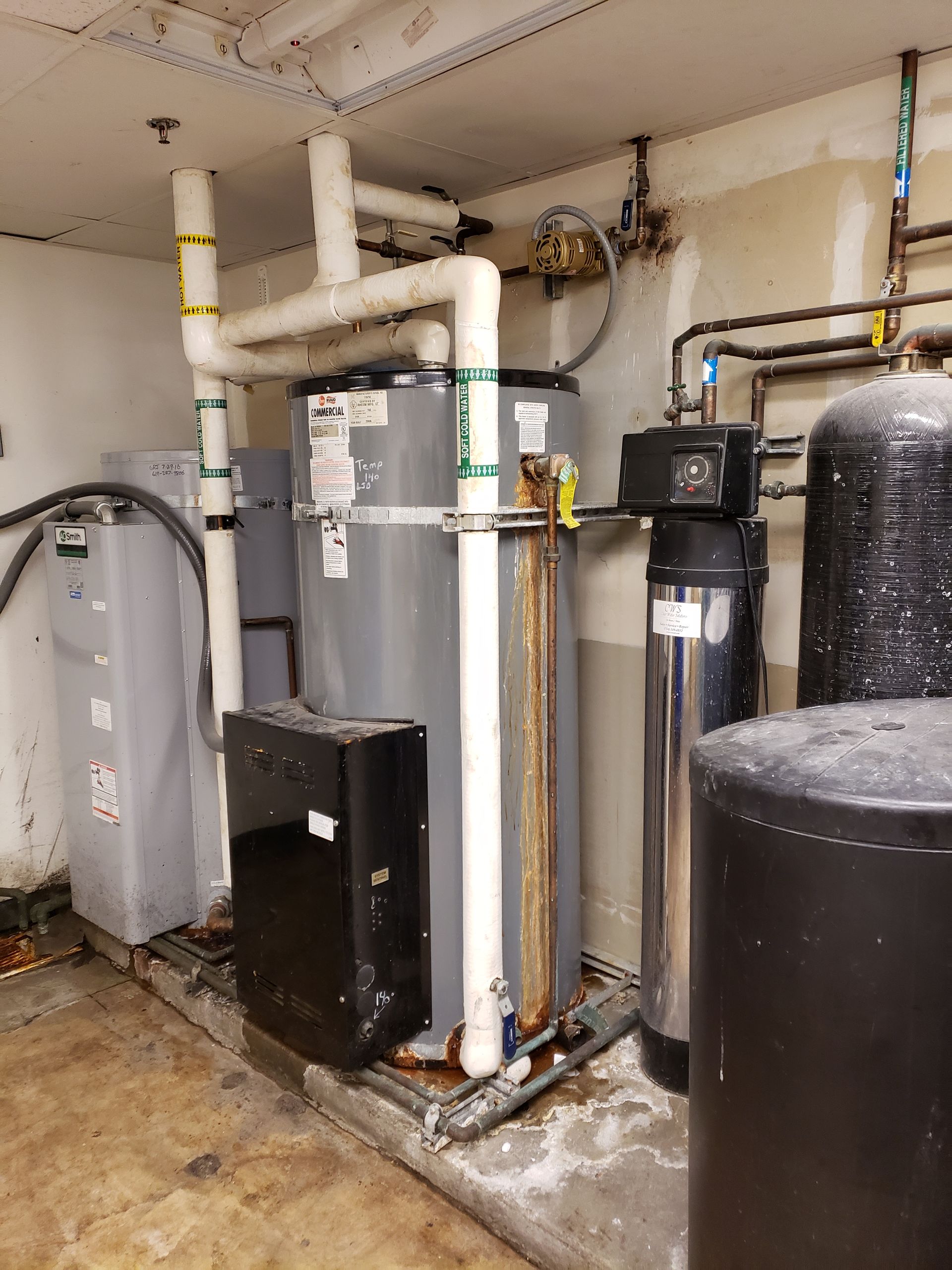 Plumbing and water heating equipment in a basement setting. Includes a water heater, pipes, and other tanks.