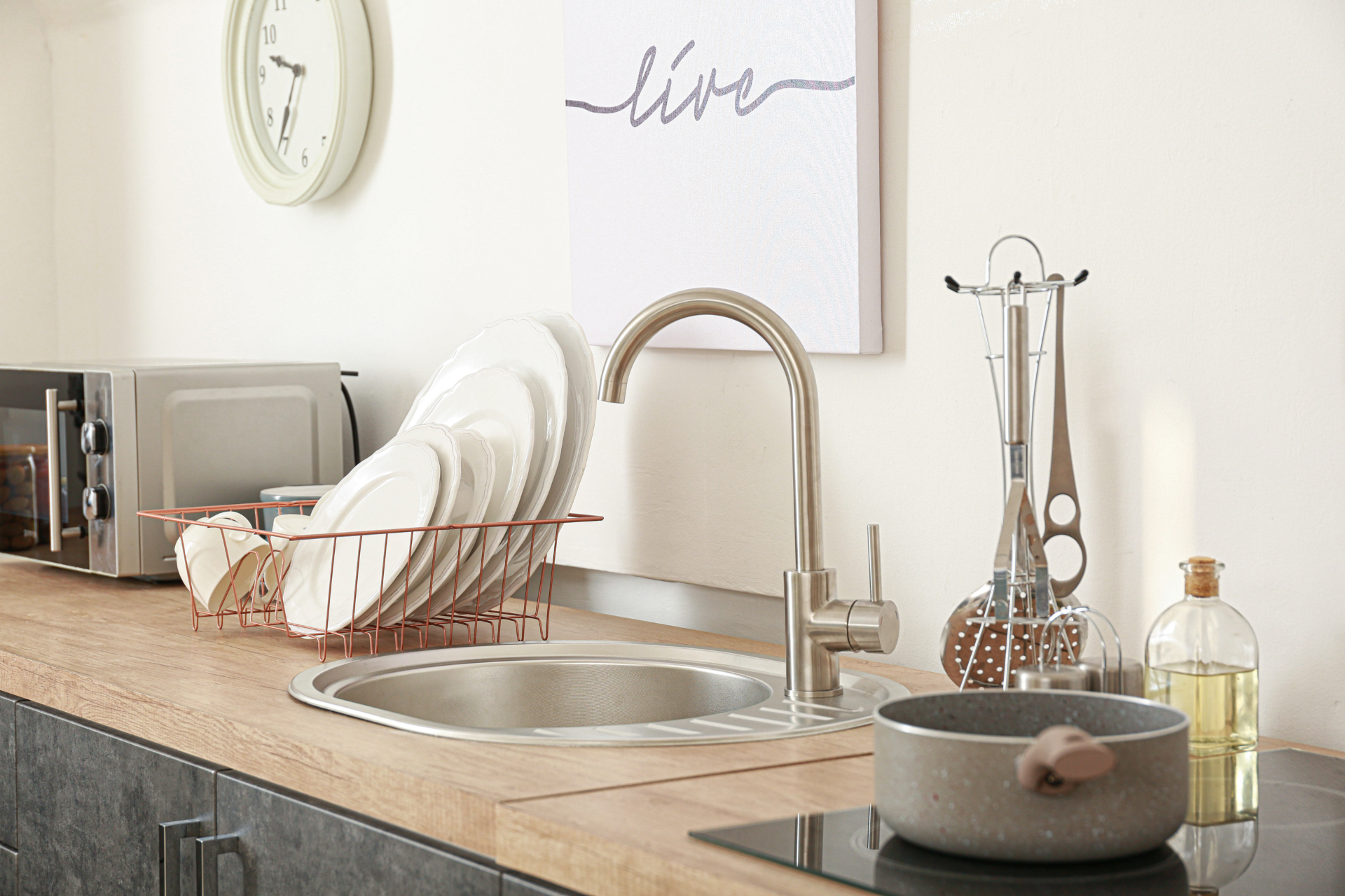 A kitchen with a sink , a clock , and a sign that says `` live ''.