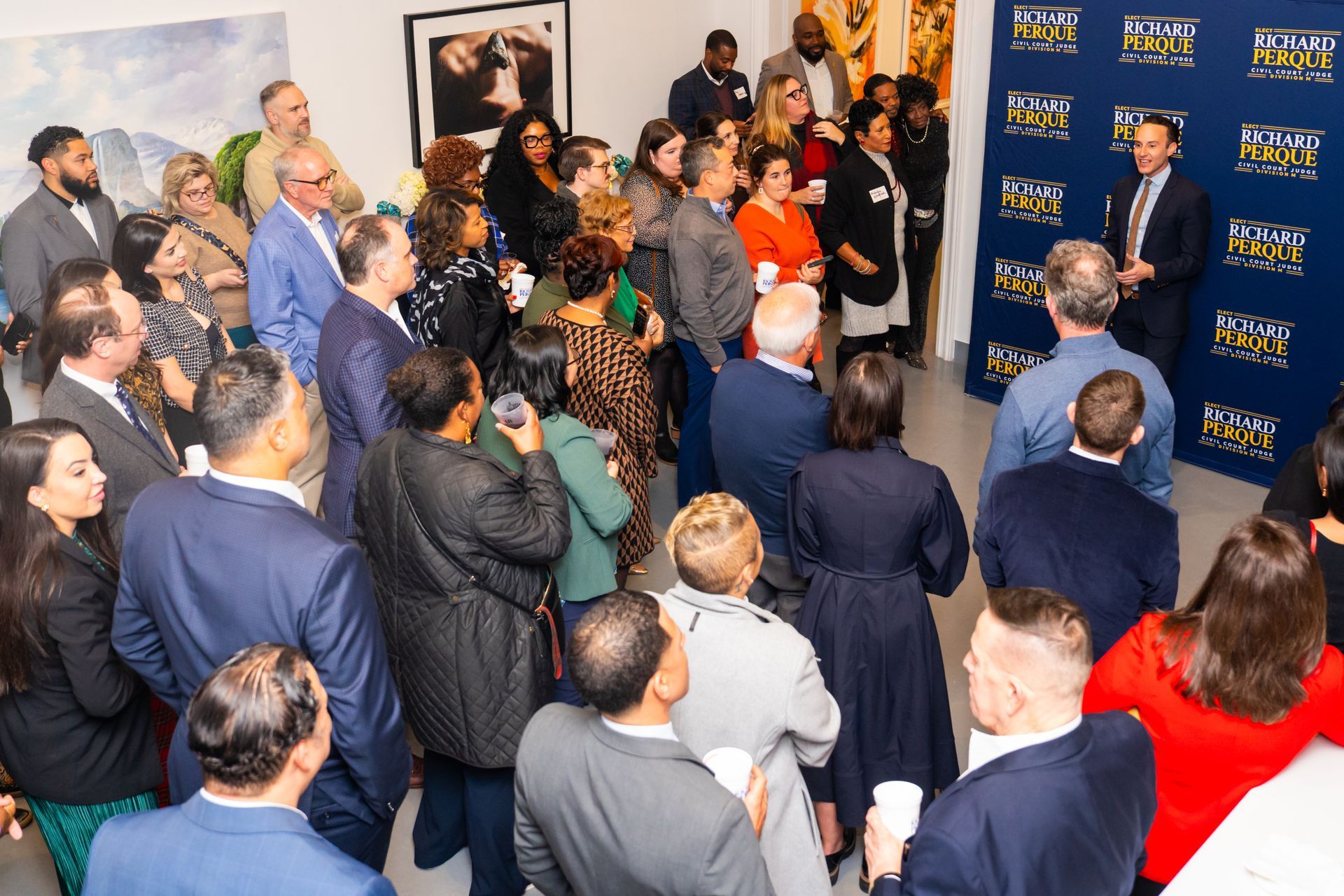 Crowd at an event, listening to a speaker in front of a branded backdrop.