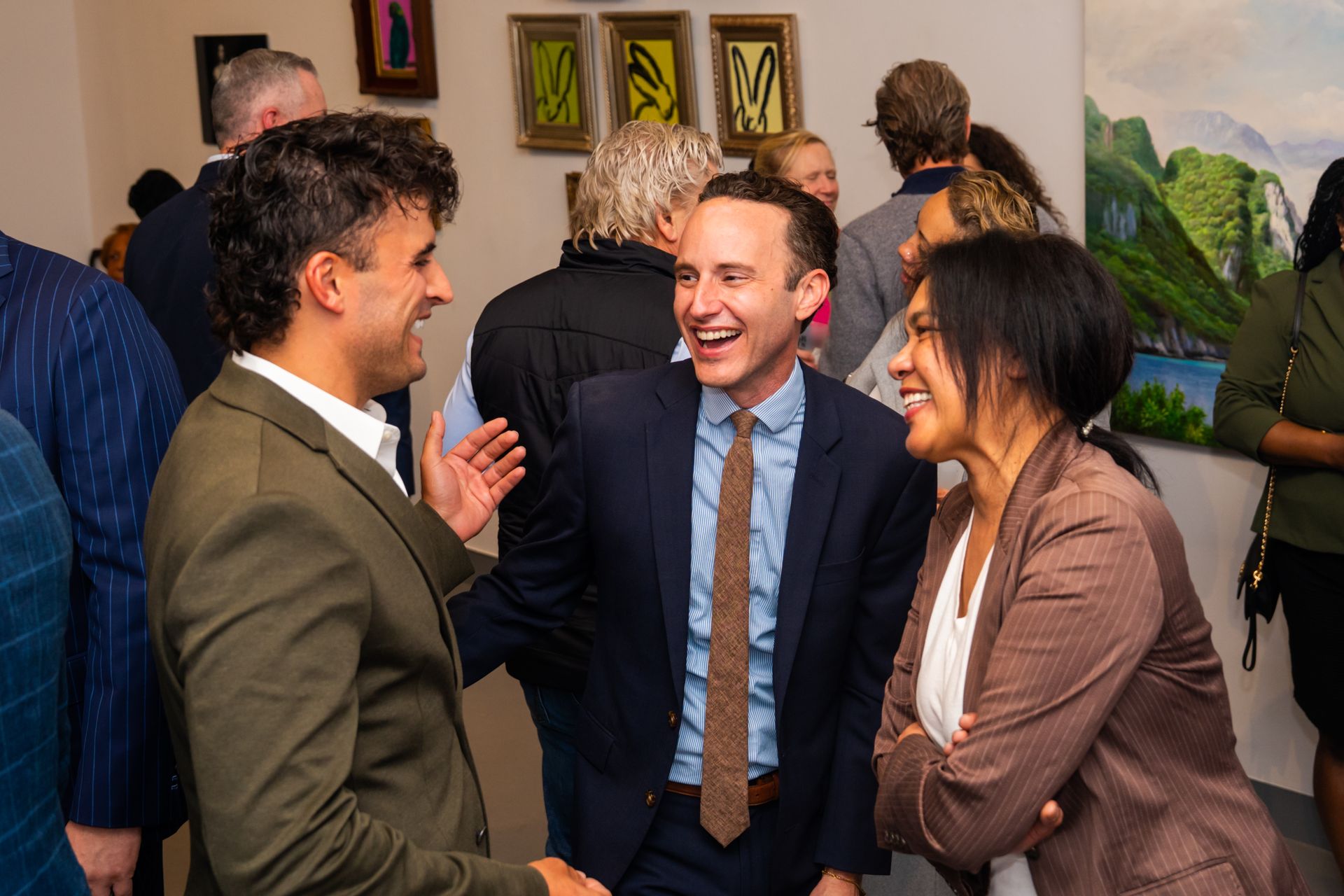 People in business attire laughing together at an art gallery.