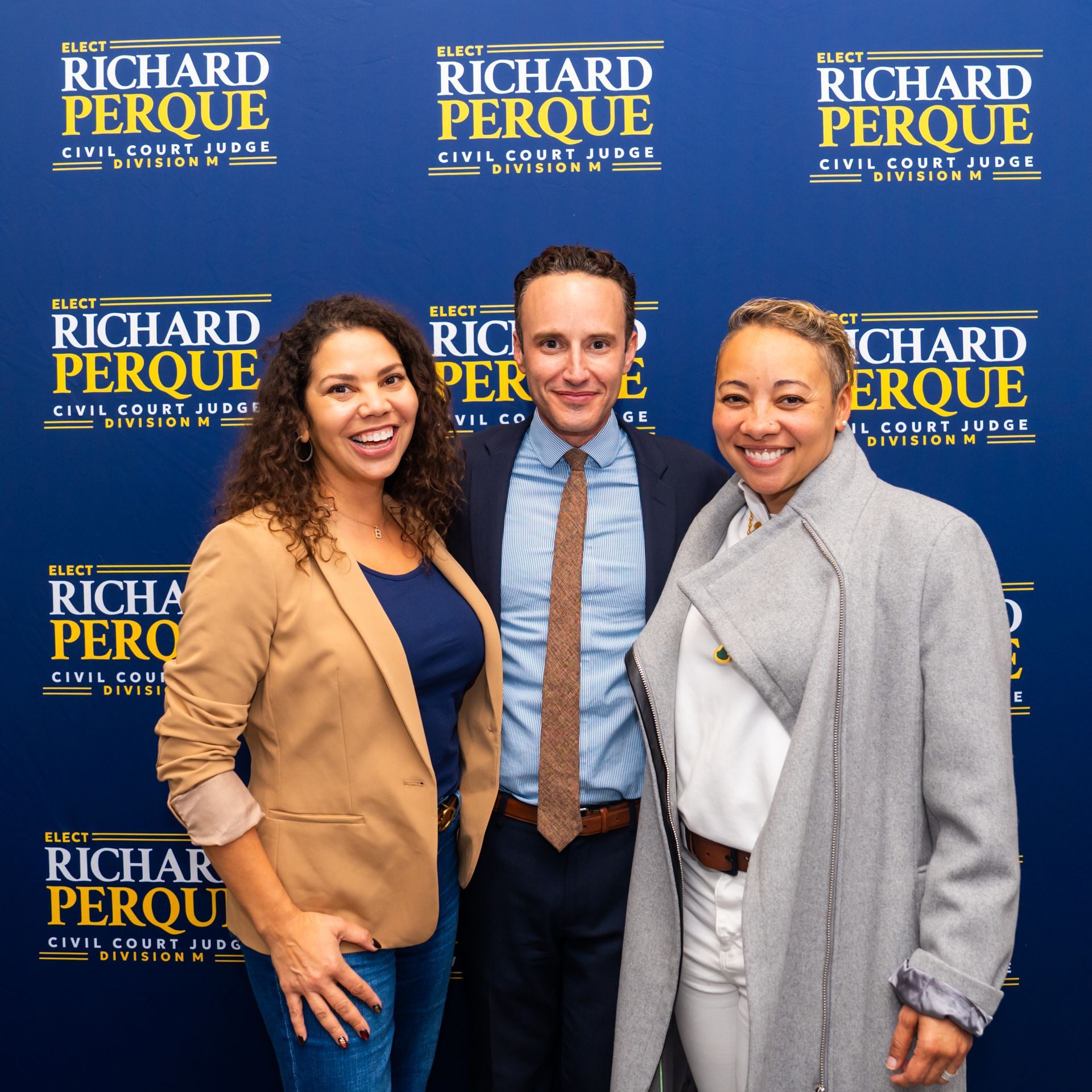 Three people smiling in front of a backdrop with a 