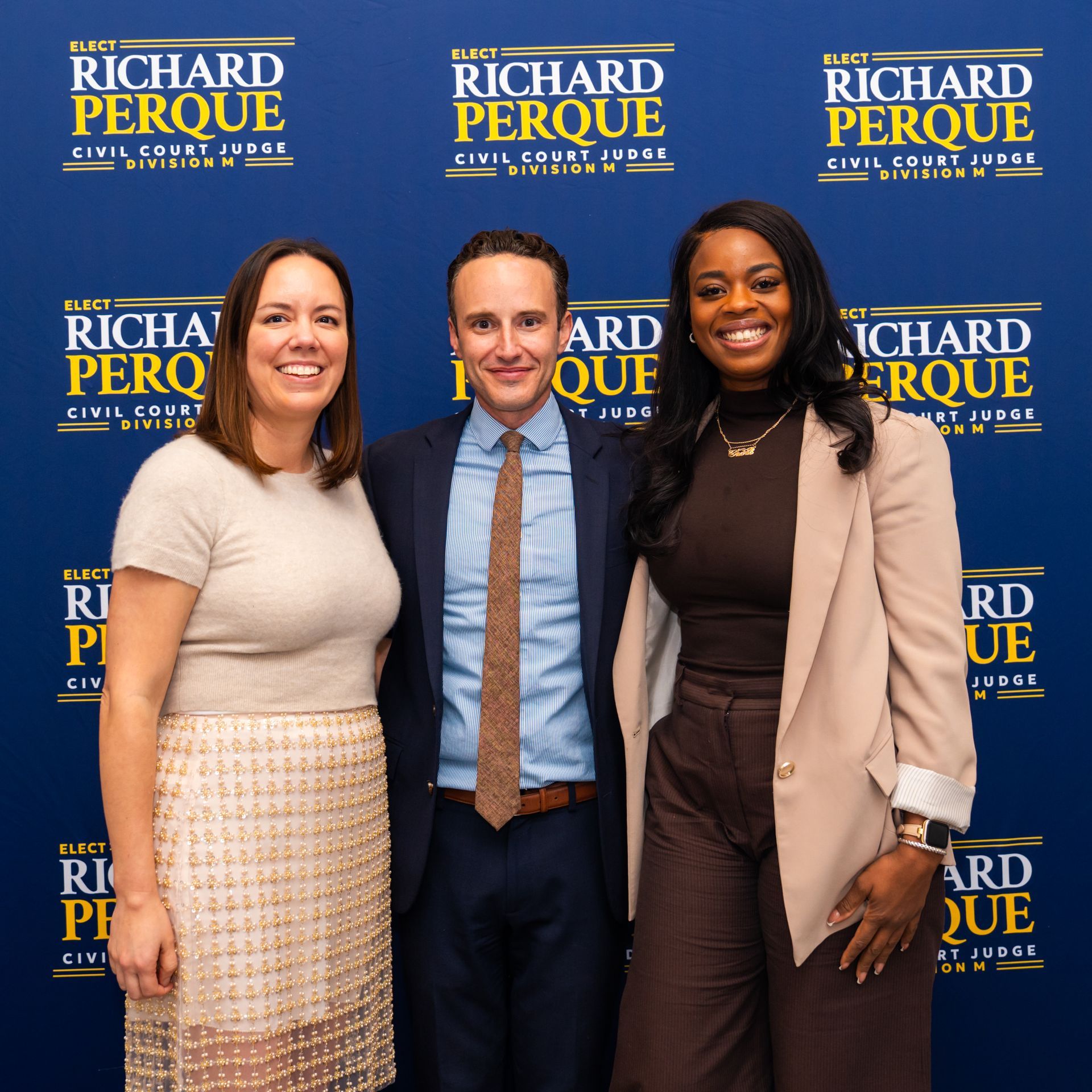 Three people pose in front of a banner for Richard Perque. The banner says 