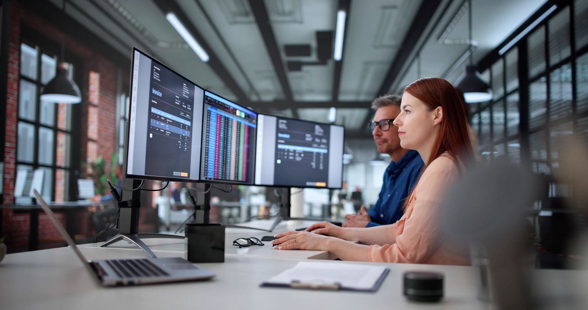 People working at computers in a dimly lit office with overhead lights.