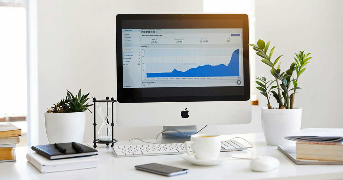 Desktop computer with a rising blue graph, surrounded by plants and office supplies.