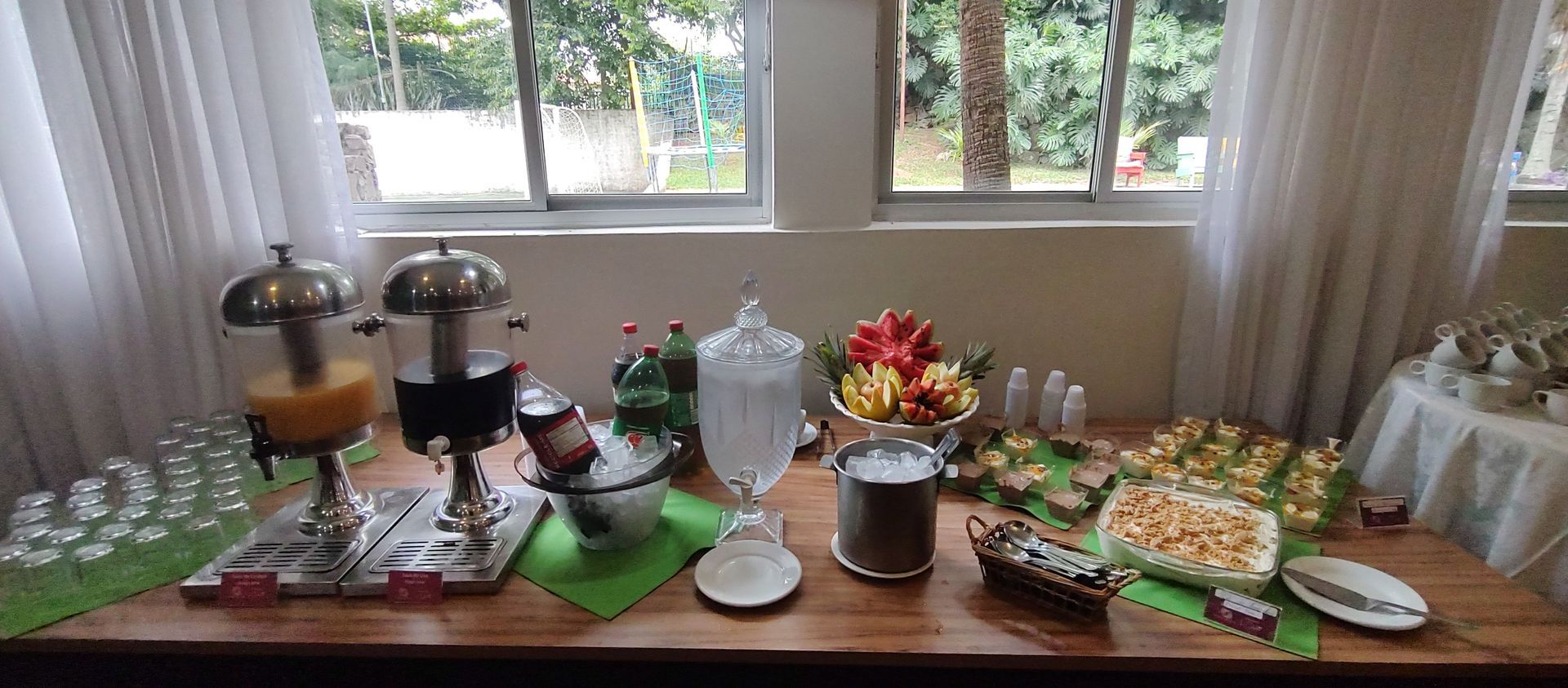 Uma mesa com uma variedade de comidas e bebidas em frente a uma janela.