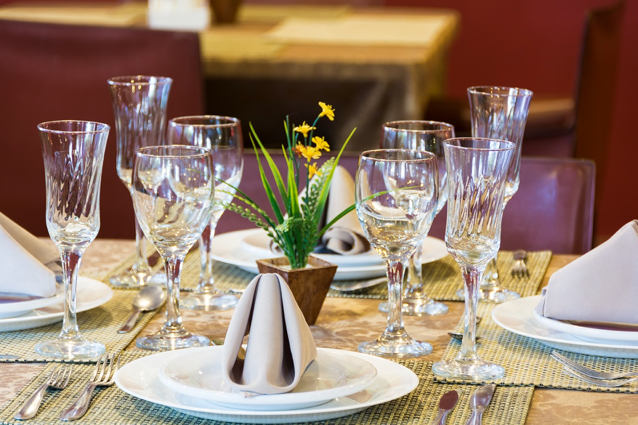 Uma mesa está posta com pratos, taças de vinho e um vaso de flores.