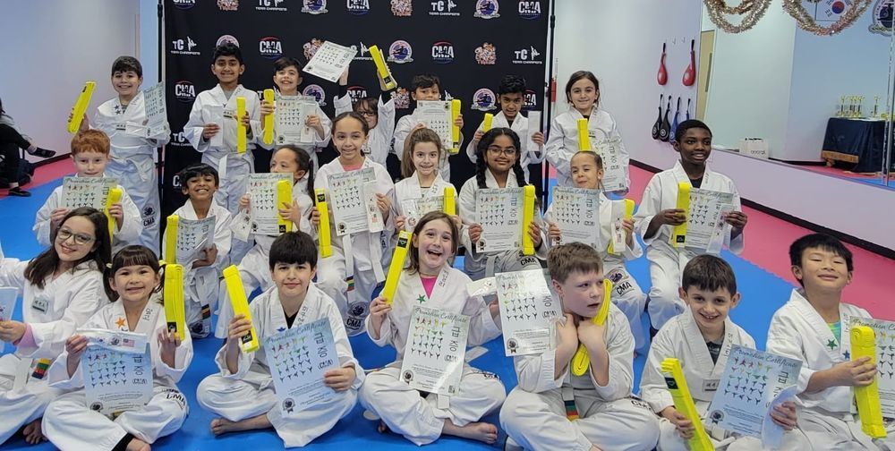 A group of children are sitting on the floor in a gym holding certificates.