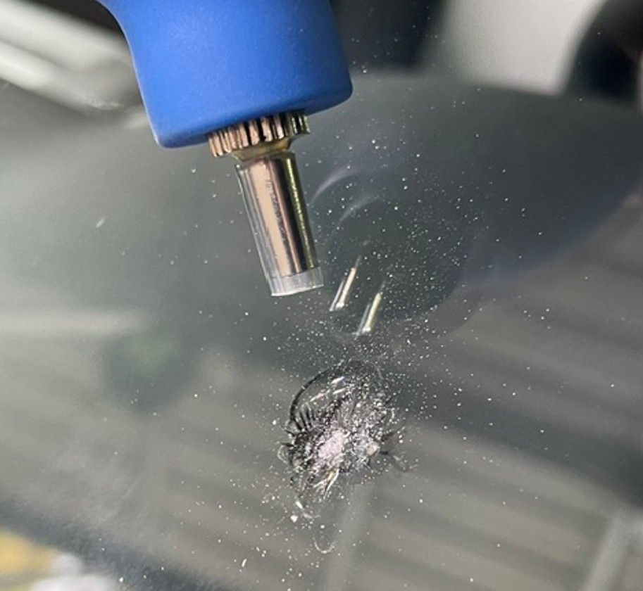 Windshield being repaired with a tool, showing damage from a rock, in a vehicle.