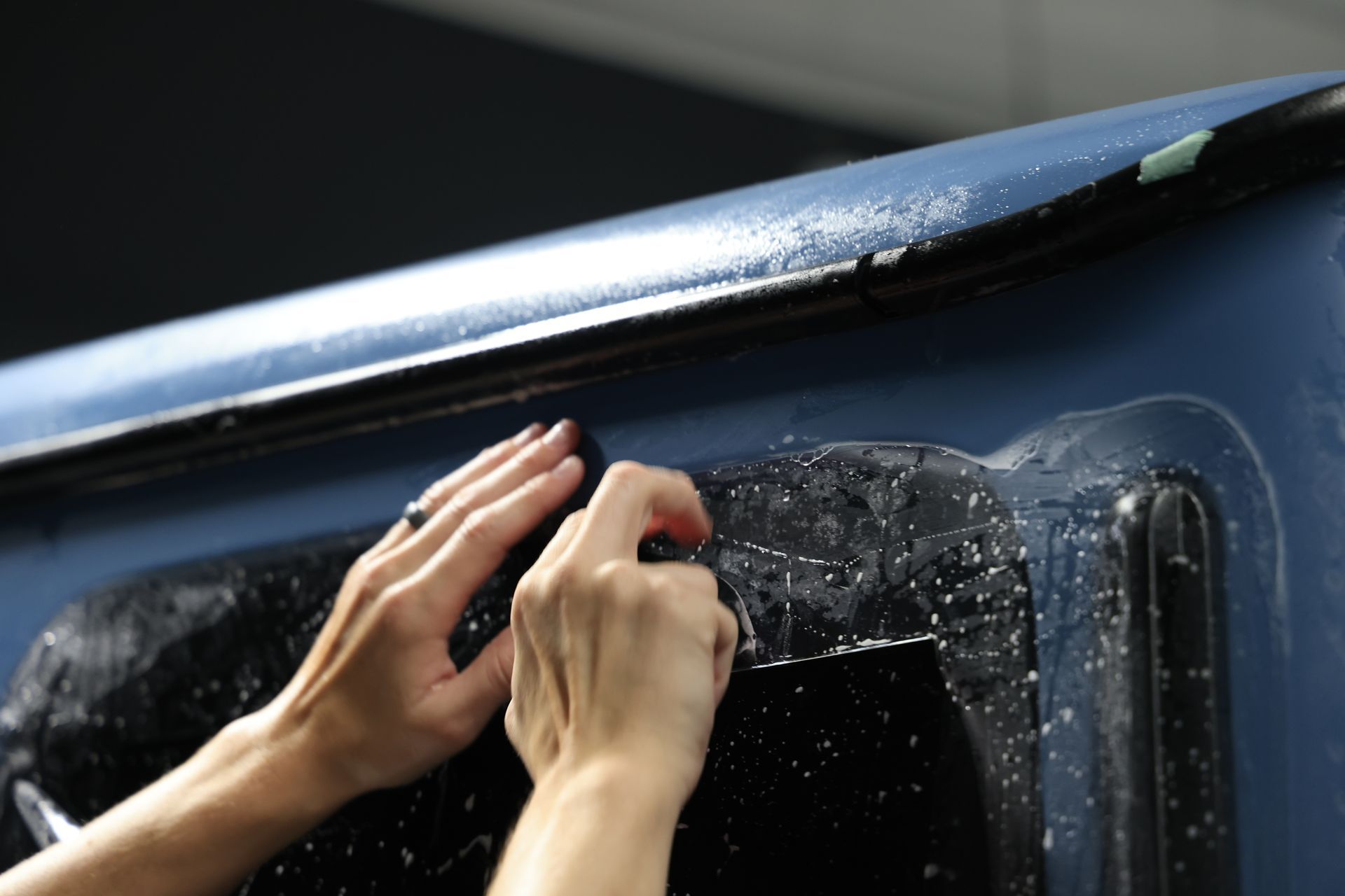 Hands applying tint film to a vehicle window, blue car, close-up.