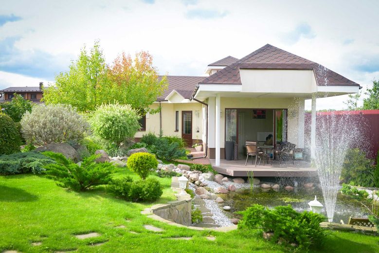 House with a landscaped yard, pond, and fountain on a sunny day.