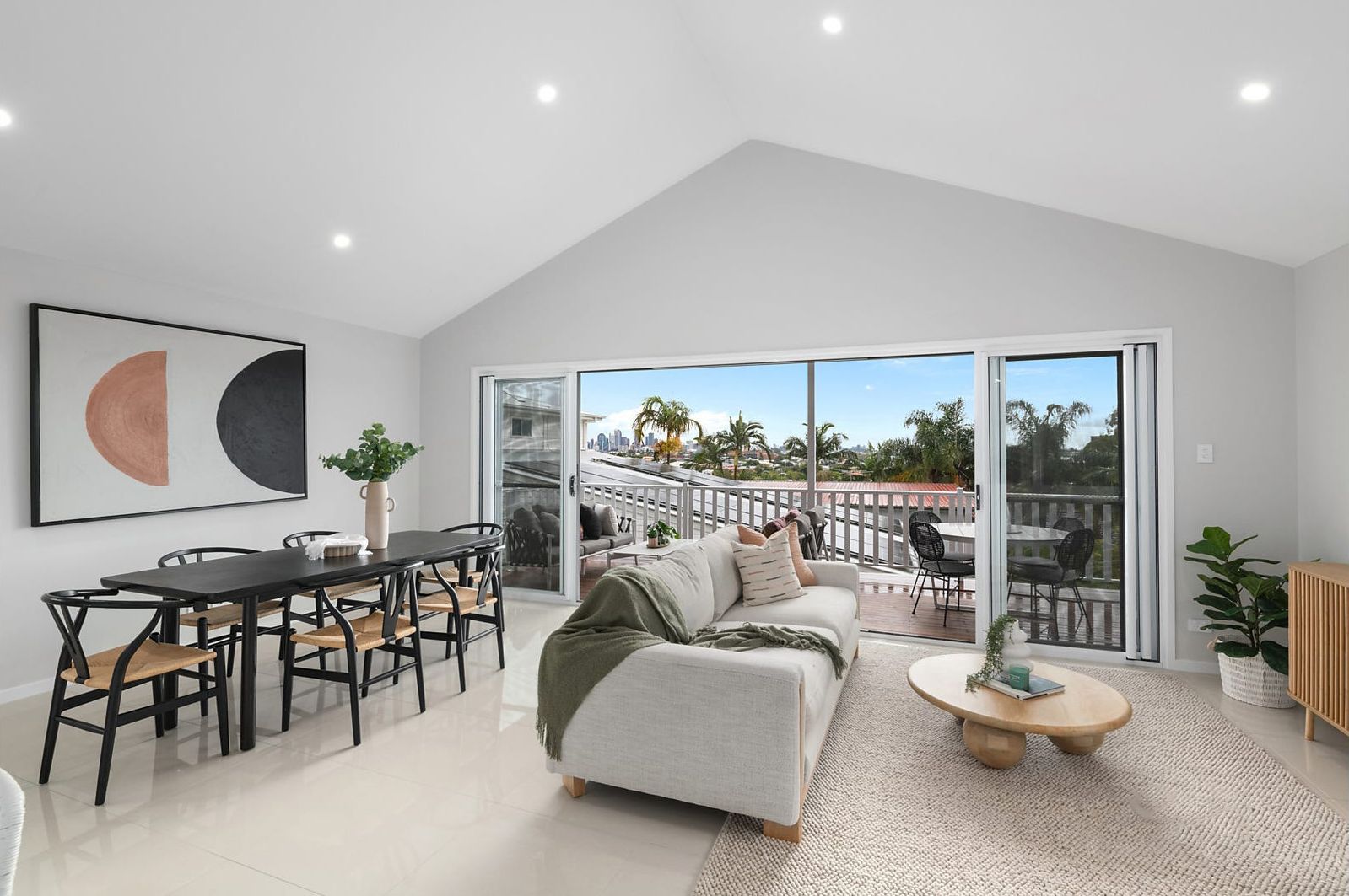 Spacious living room with dining area, balcony access, and modern furnishings. Features a sofa, dining table, and abstract artwork.
