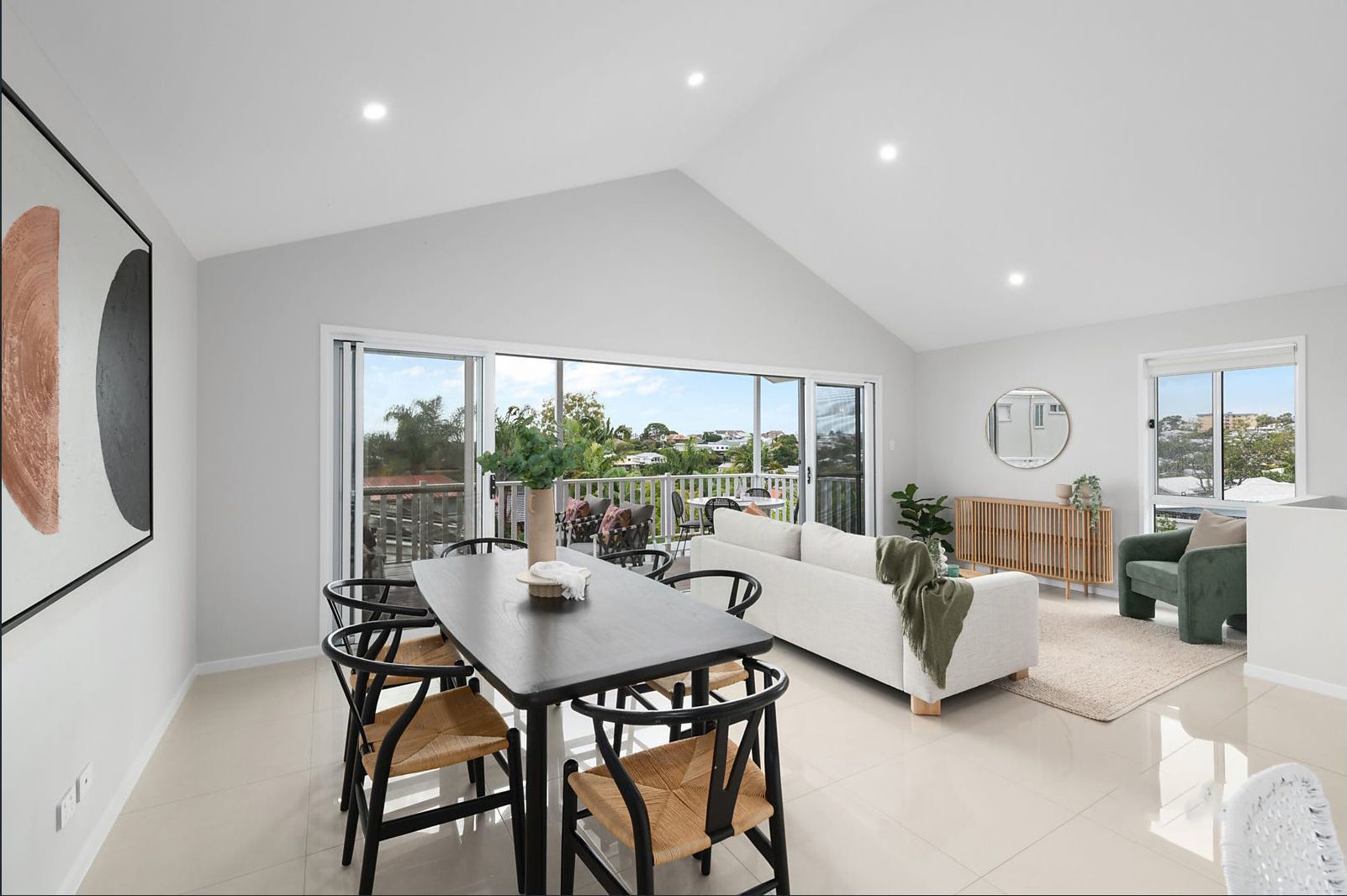 A bright, modern dining and living room. Features a dark table with black chairs, white couch, and large glass doors with an outdoor view.