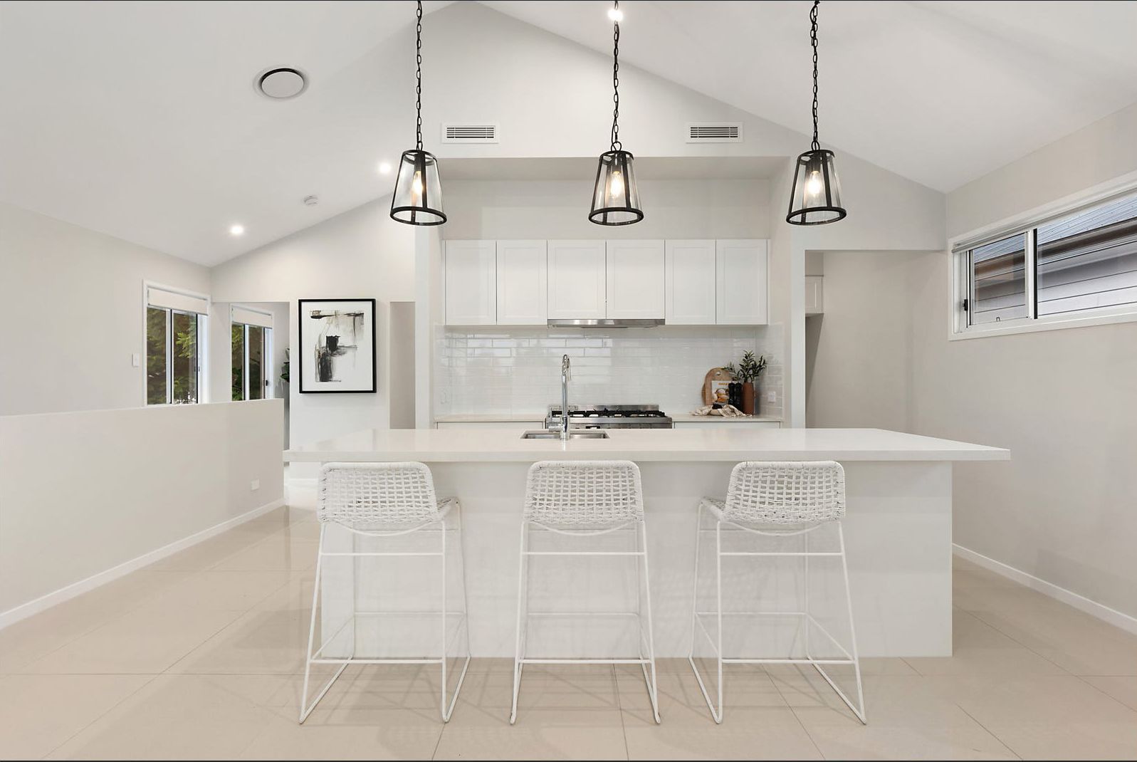 Bright, modern kitchen with white cabinets, island with three bar stools, and pendant lights.