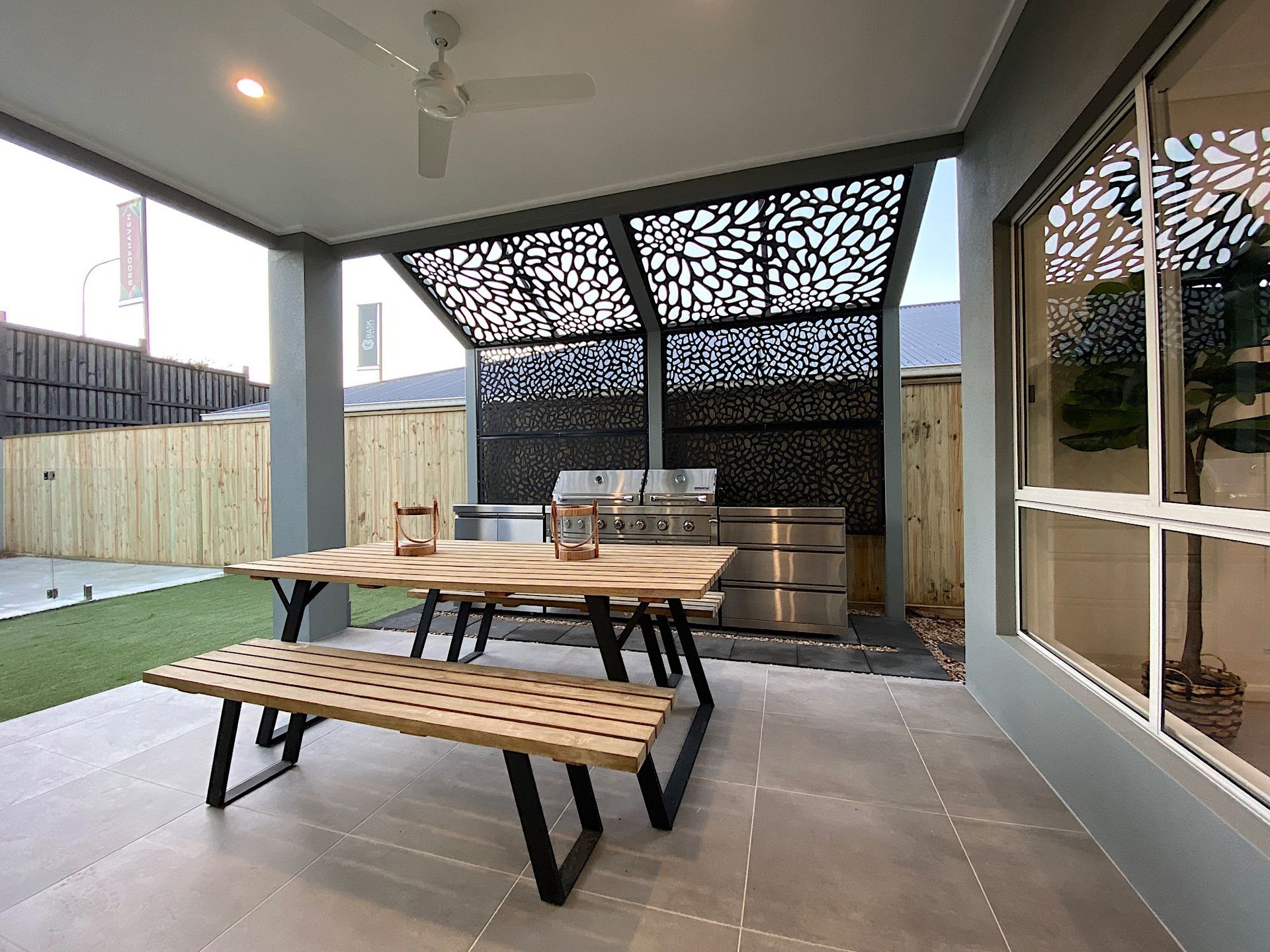 Outdoor patio with a grill BBQ, dining table, and decorative privacy screen under a covered area.