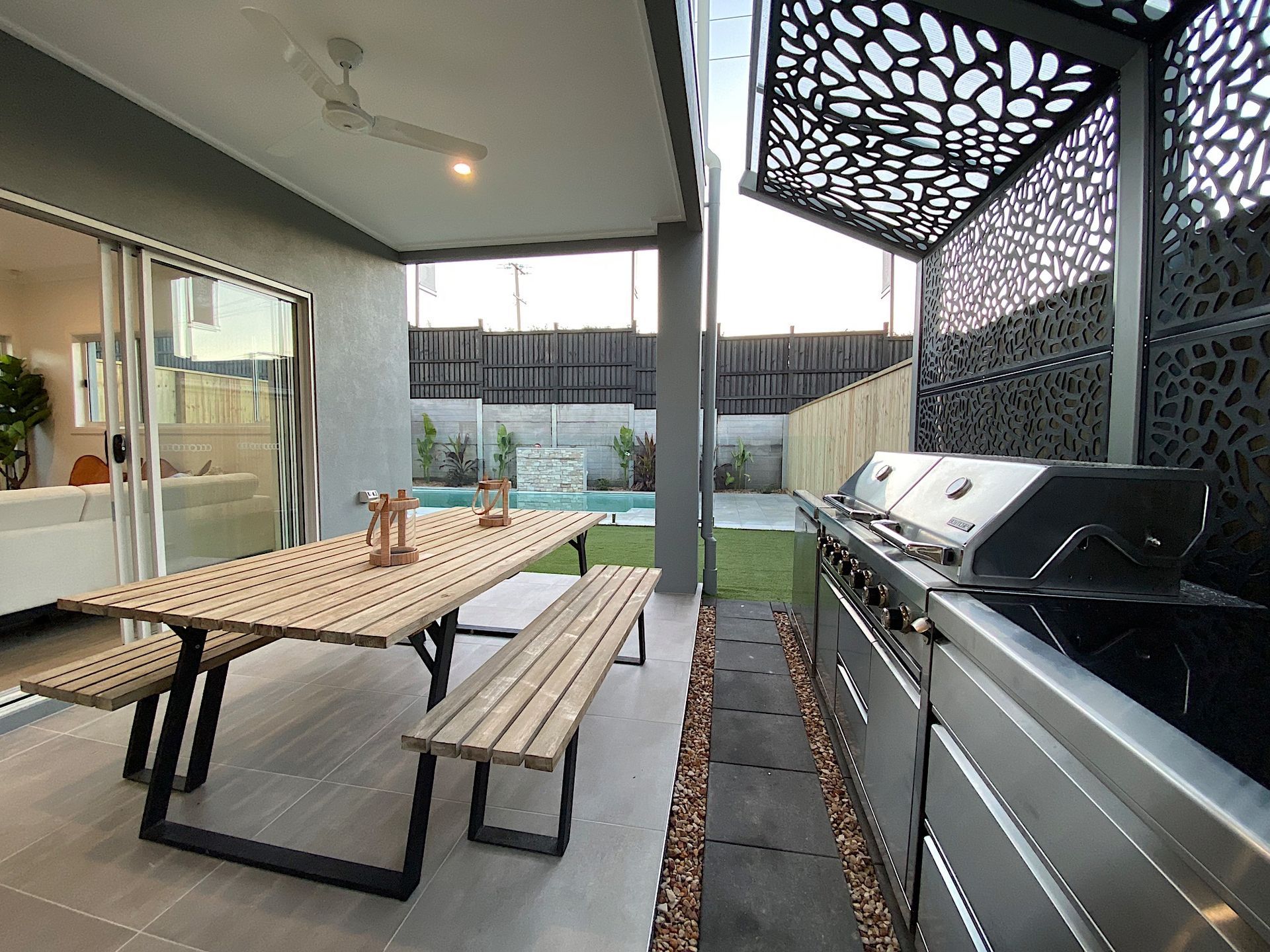 Outdoor patio with dining table, benches, and grill. Features pool in the background.