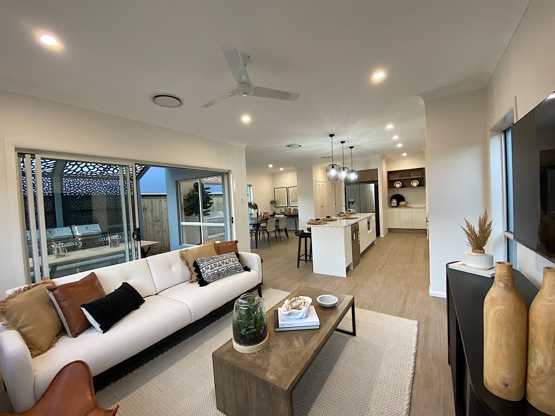 Open-concept living space with white sofa, kitchen island, and sliding door to patio. Neutral tones.