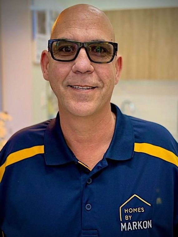 Bald man with glasses, wearing a navy blue polo shirt with gold stripes and logo, smiling. Ken Ford