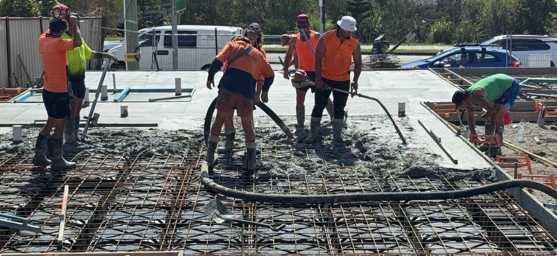 Construction workers pouring concrete on a foundation, with reinforcing bars visible.