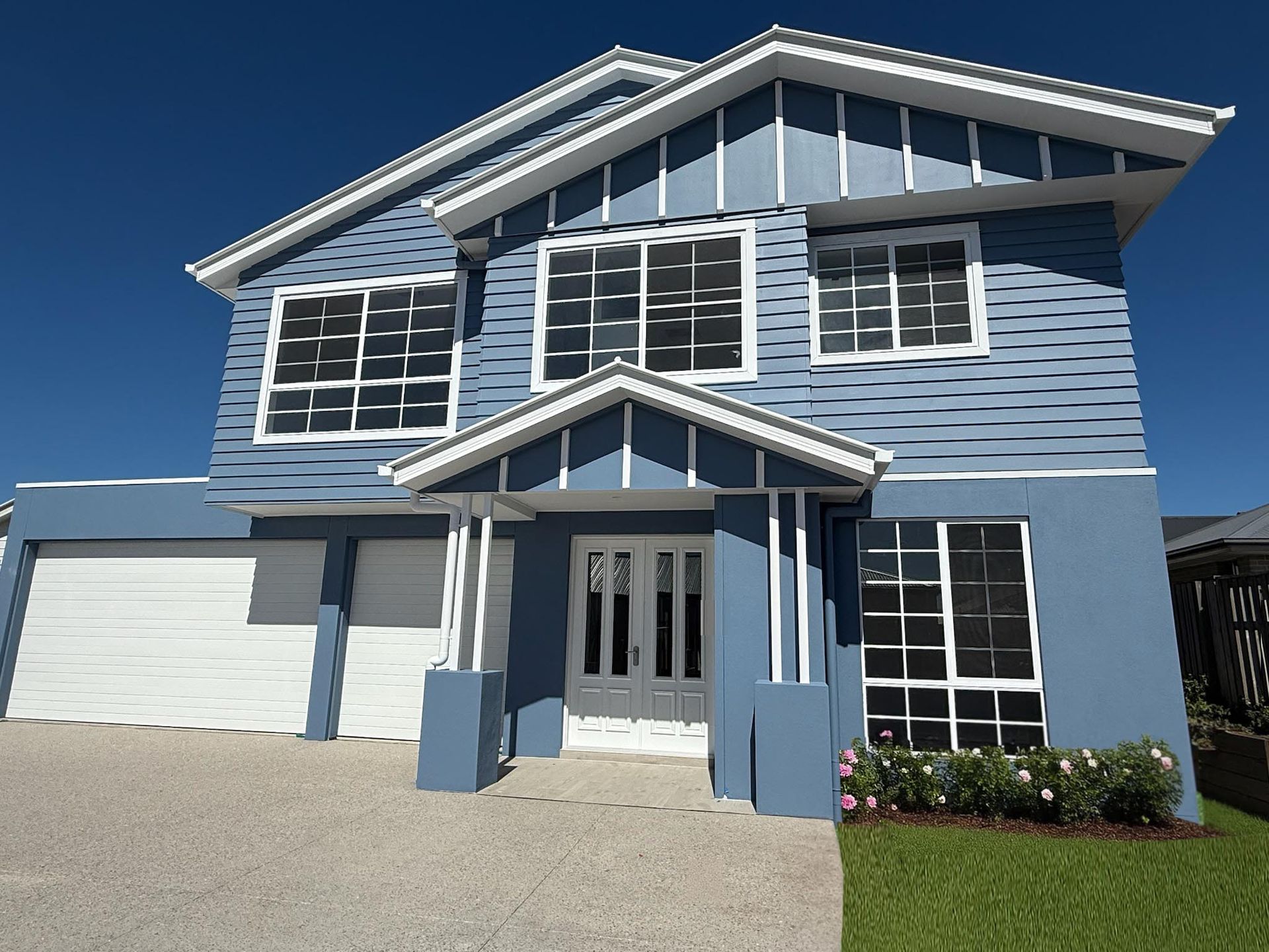 Two-story blue house with white trim, garage, and front door under a clear sky.