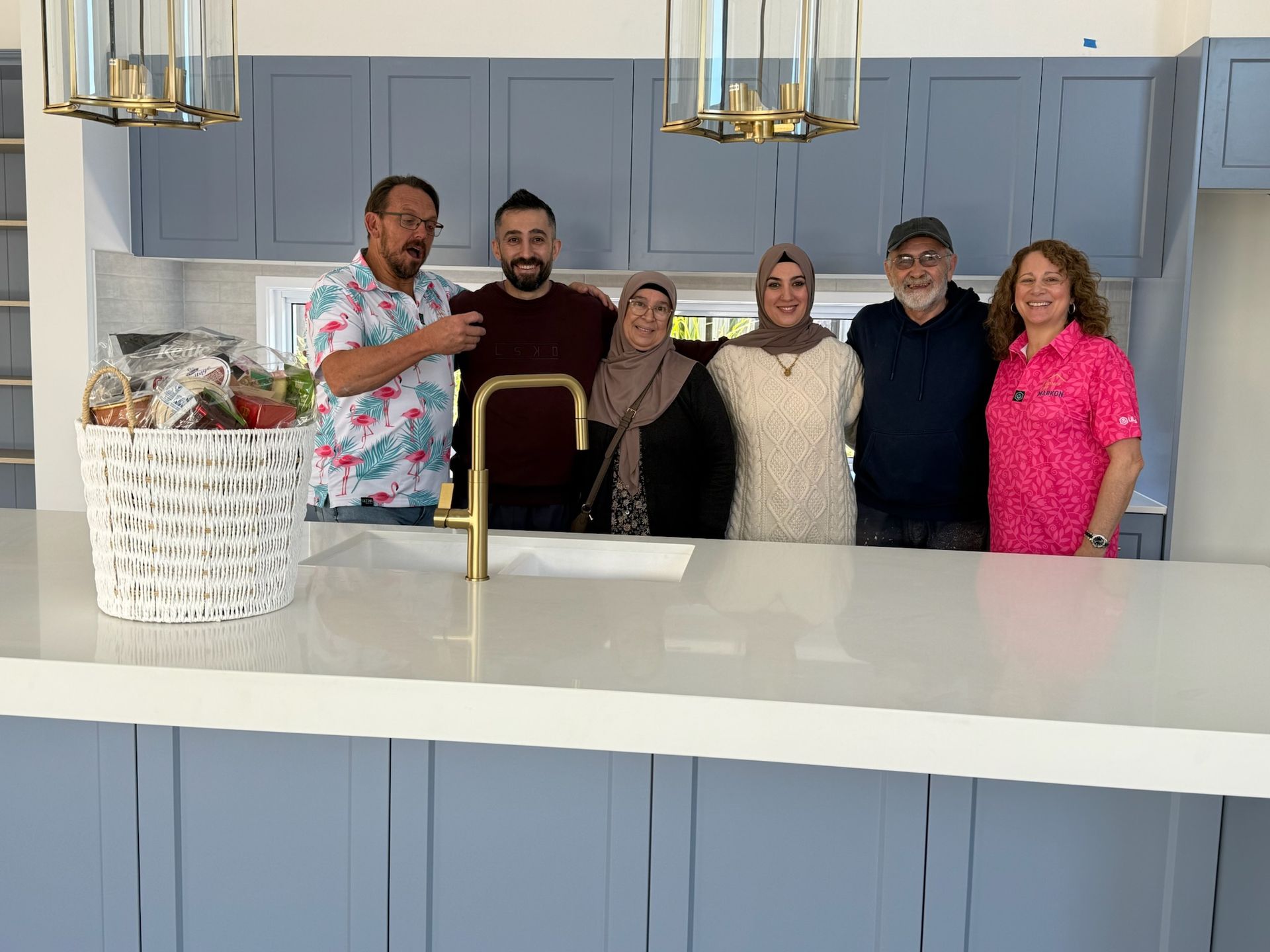 Four people pose in a kitchen with blue cabinets. They are smiling, arms around each other.