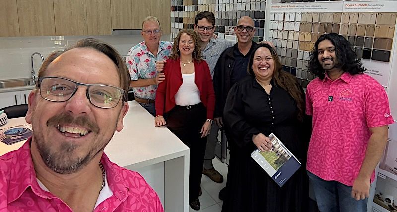 Group of people smiling in a showroom. One man takes a selfie. Samples are displayed on the wall at the Markon Group. 