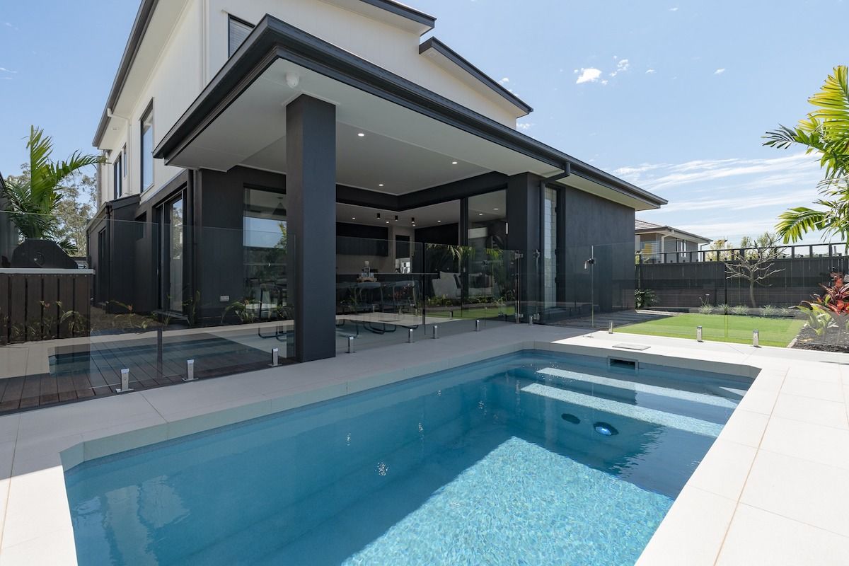 Modern white house with a long, dark pool reflecting the blue sky.
