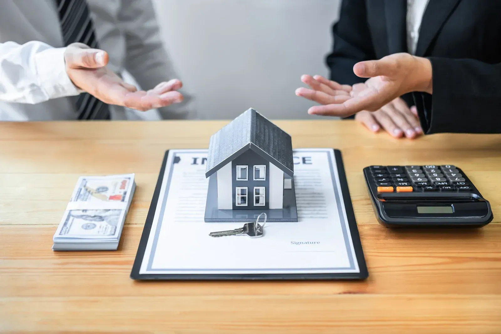 A man and a woman are sitting at a table with a model house and a calculator.