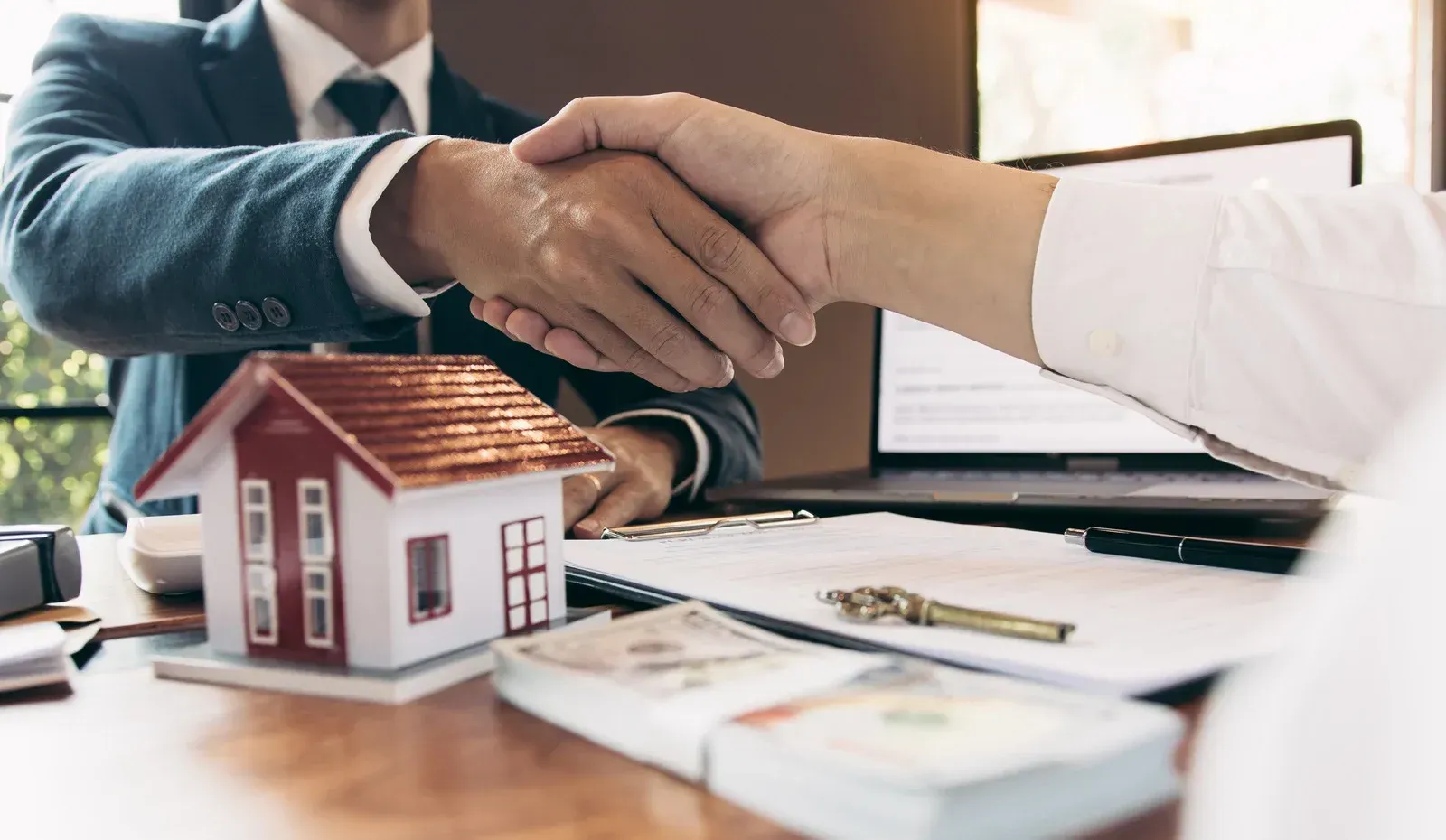 A man in a suit and tie is shaking hands with a woman in front of a model house.