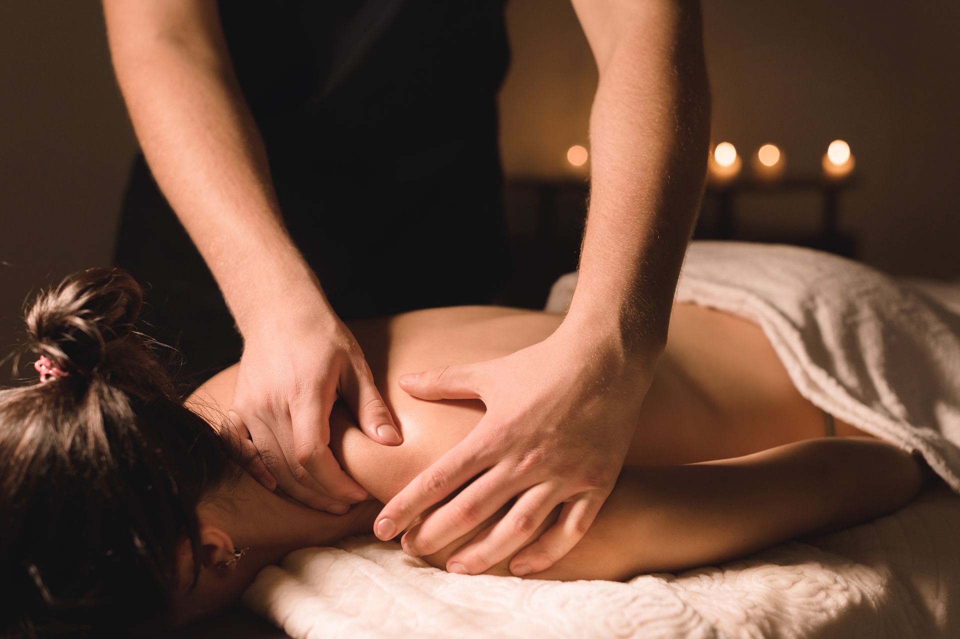 Eine Massagetherapeutin massiert den Rücken einer Kundin in einem abgedunkelten Spa-Raum bei Kerzenschein.