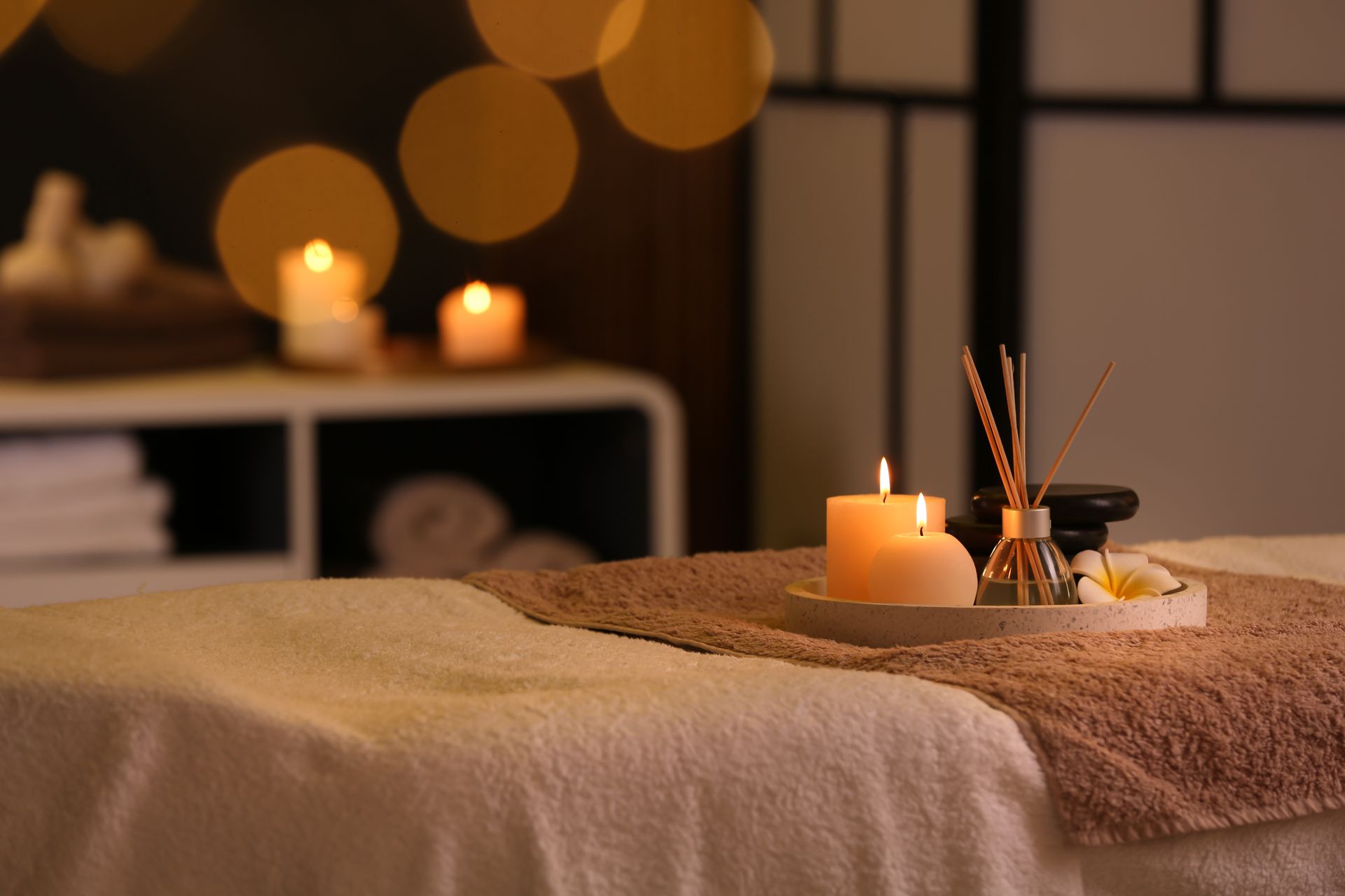 Spa-Massageliege mit Kerzen, warmem Licht und ätherischen Ölen in einem abgedunkelten Raum