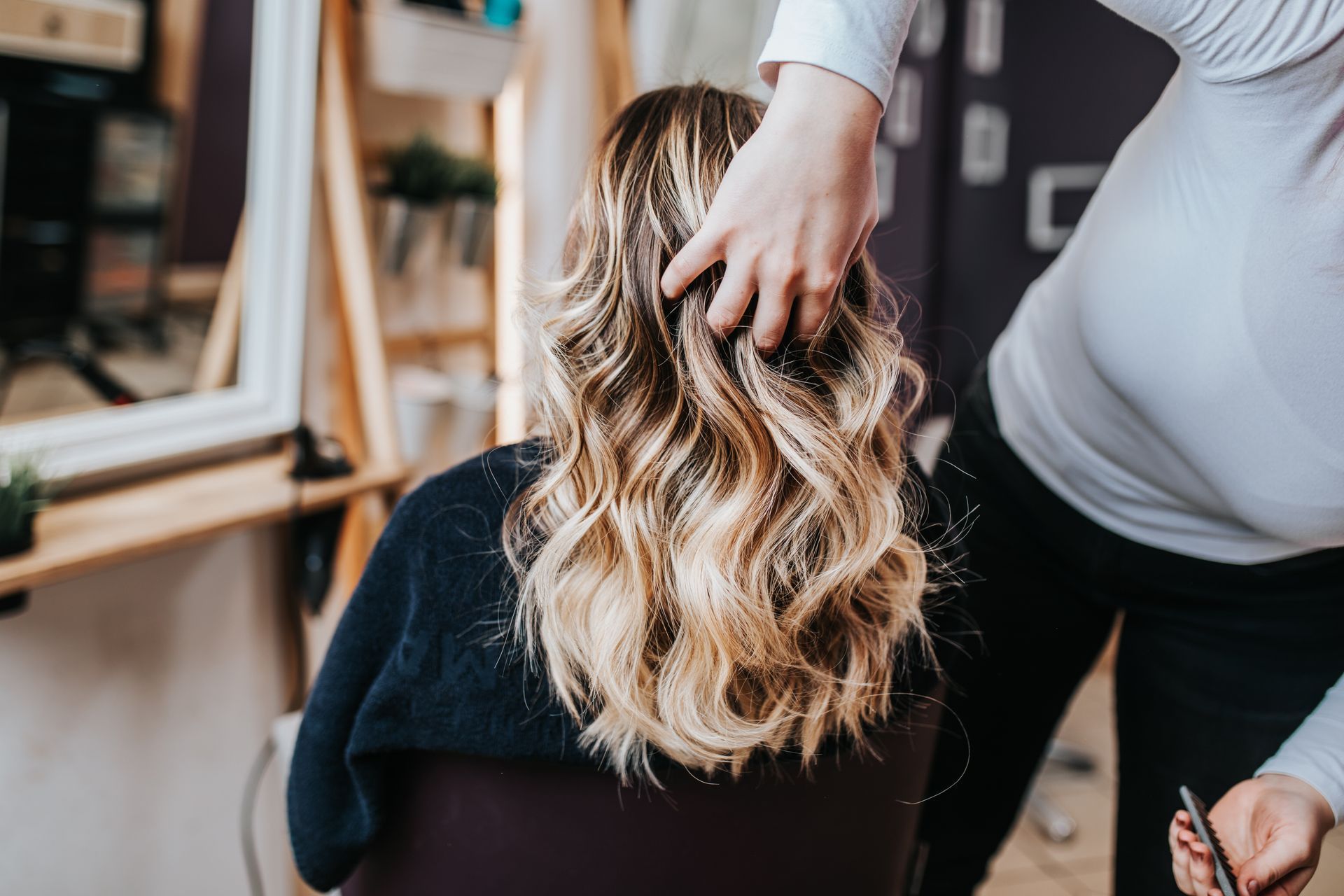 Eine Stylistin richtet welliges blondes Haar auf einem Friseurstuhl.