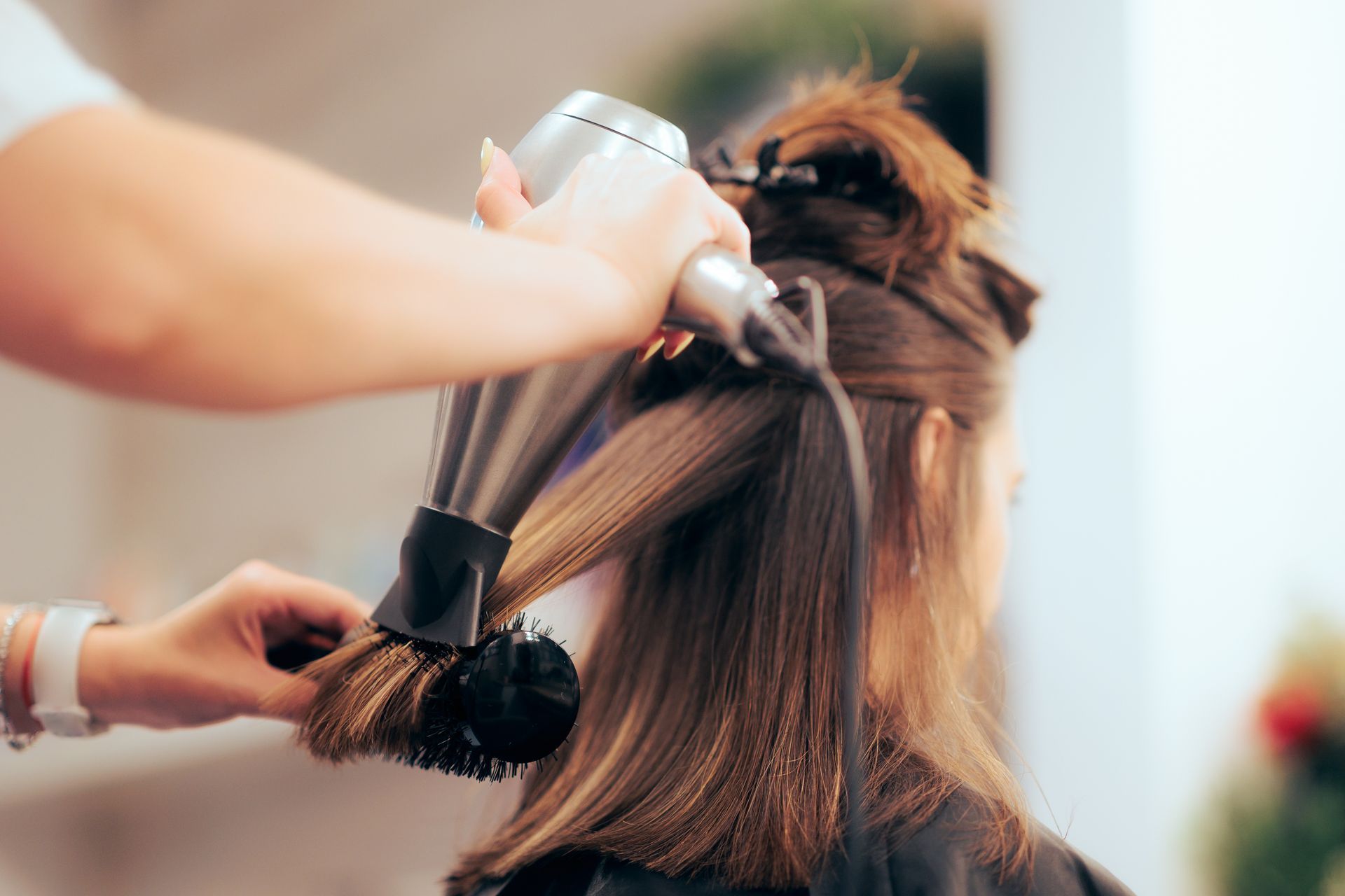 Eine Friseurin föhnt einer Kundin im Salon die braunen Haare.