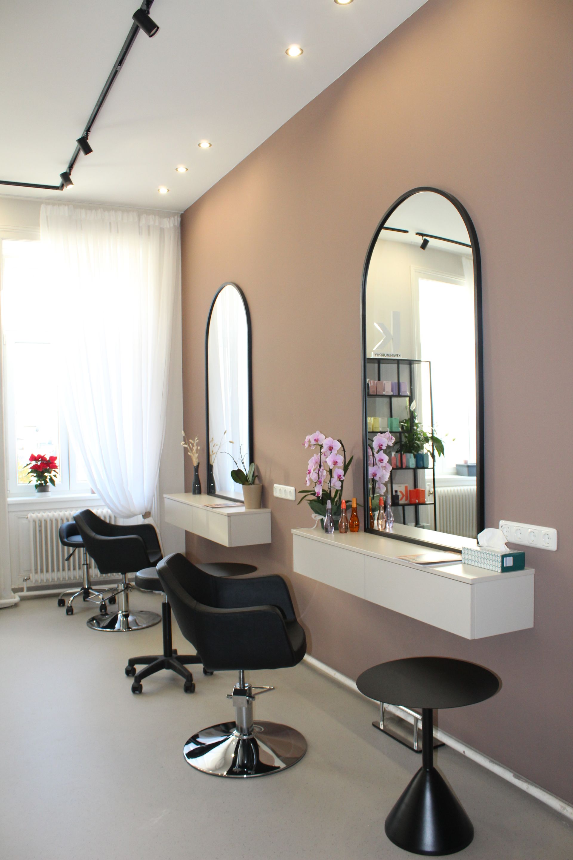 Friseursalon mit Frisierstühlen, Spiegeln und einer Reihe von Arbeitsplätzen in einem sanft beleuchteten Raum