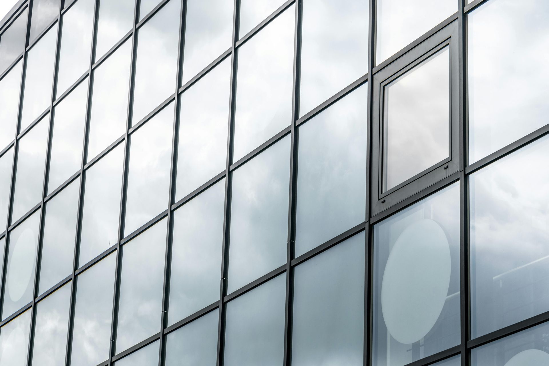 A close up of a building with a lot of windows and a cloudy sky reflected in the windows.