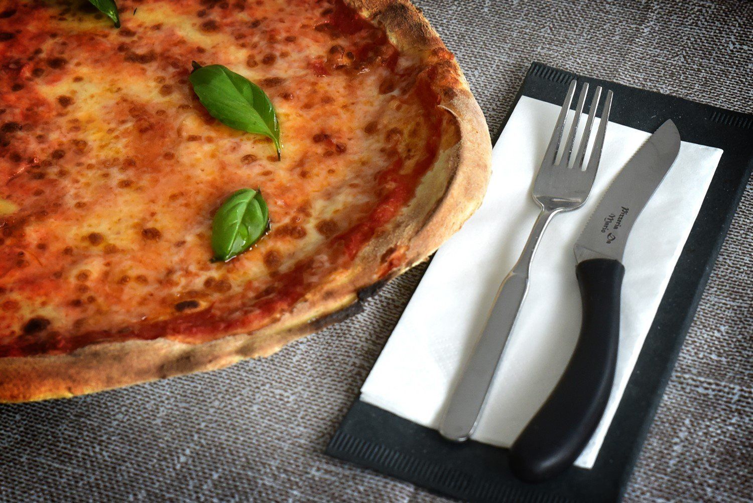 Pizza margherita apparecchiata con forchetta e coltello